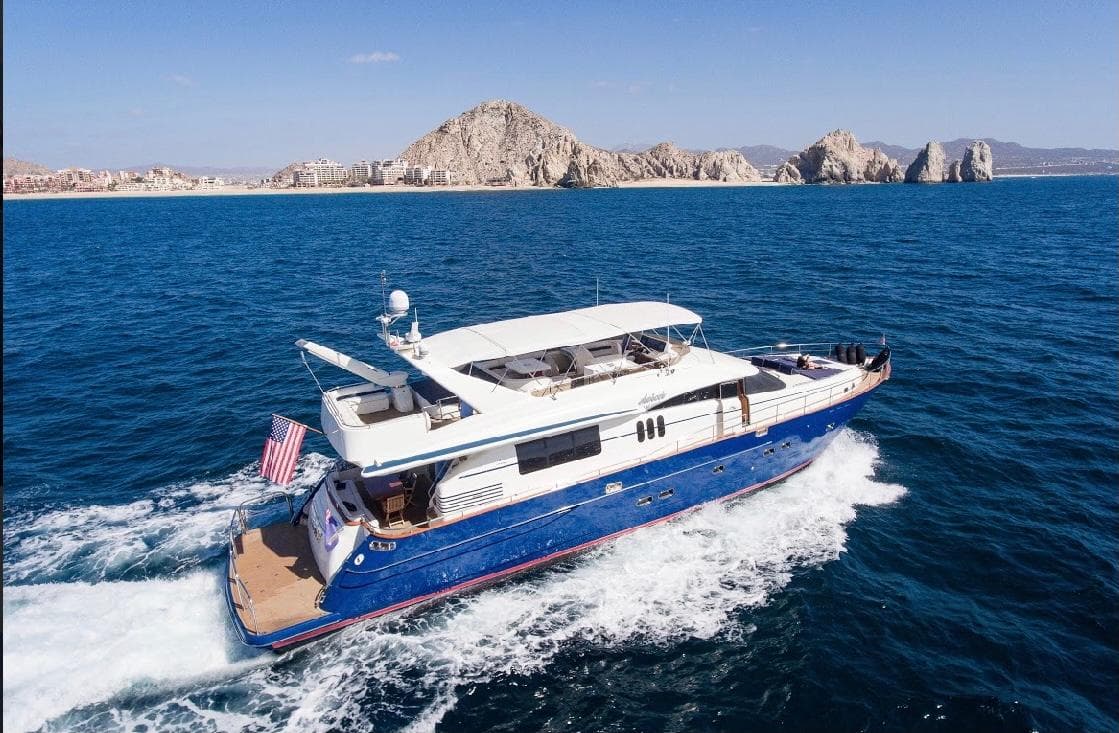 2002 Viking Princess motor yacht cruising near rocky coastline under clear blue sky.
