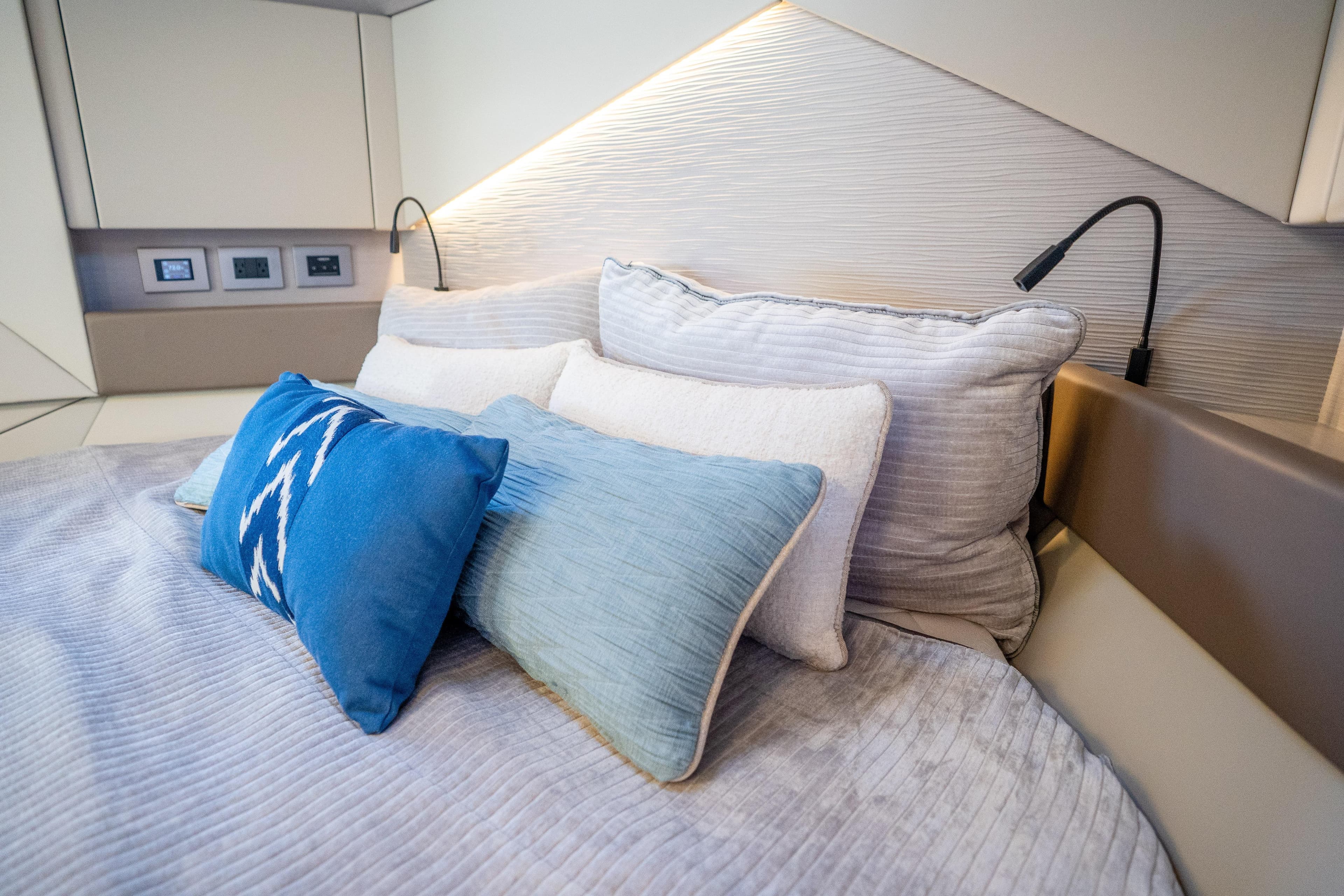 Luxurious bedroom interior of 2024 Pershing 7X yacht with plush pillows and modern lighting.