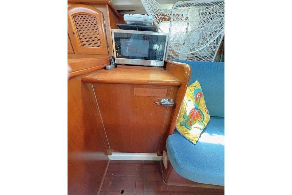 Interior of 1998 Beneteau 381 yacht with microwave, wooden cabinetry, and colorful cushion.