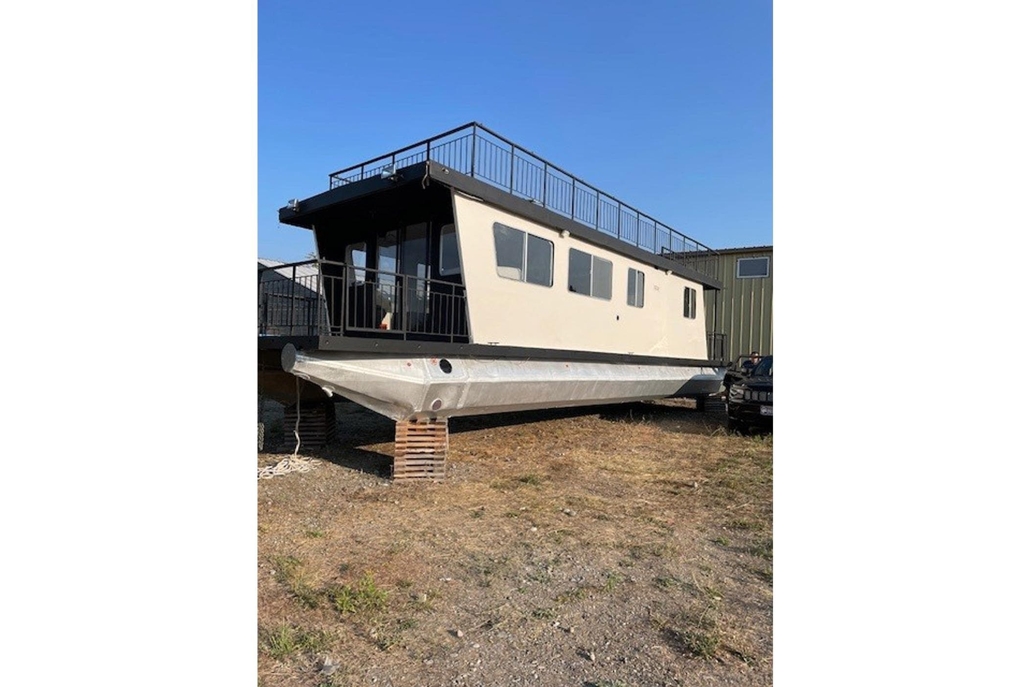 1985 Three Buoys houseboat on land, beige exterior, upper deck railing, clear sky.