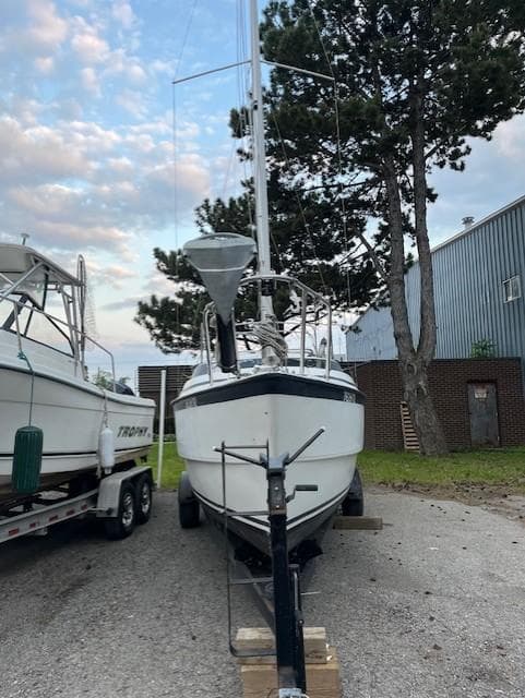 2002 MacGregor 26X sailboat on trailer, parked outdoors near trees and building.