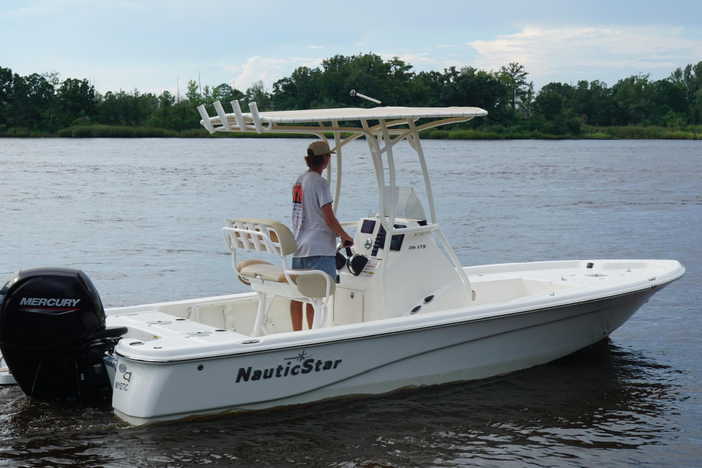 2023 NauticStar 215XTS boat on a calm river, featuring a Mercury outboard motor.