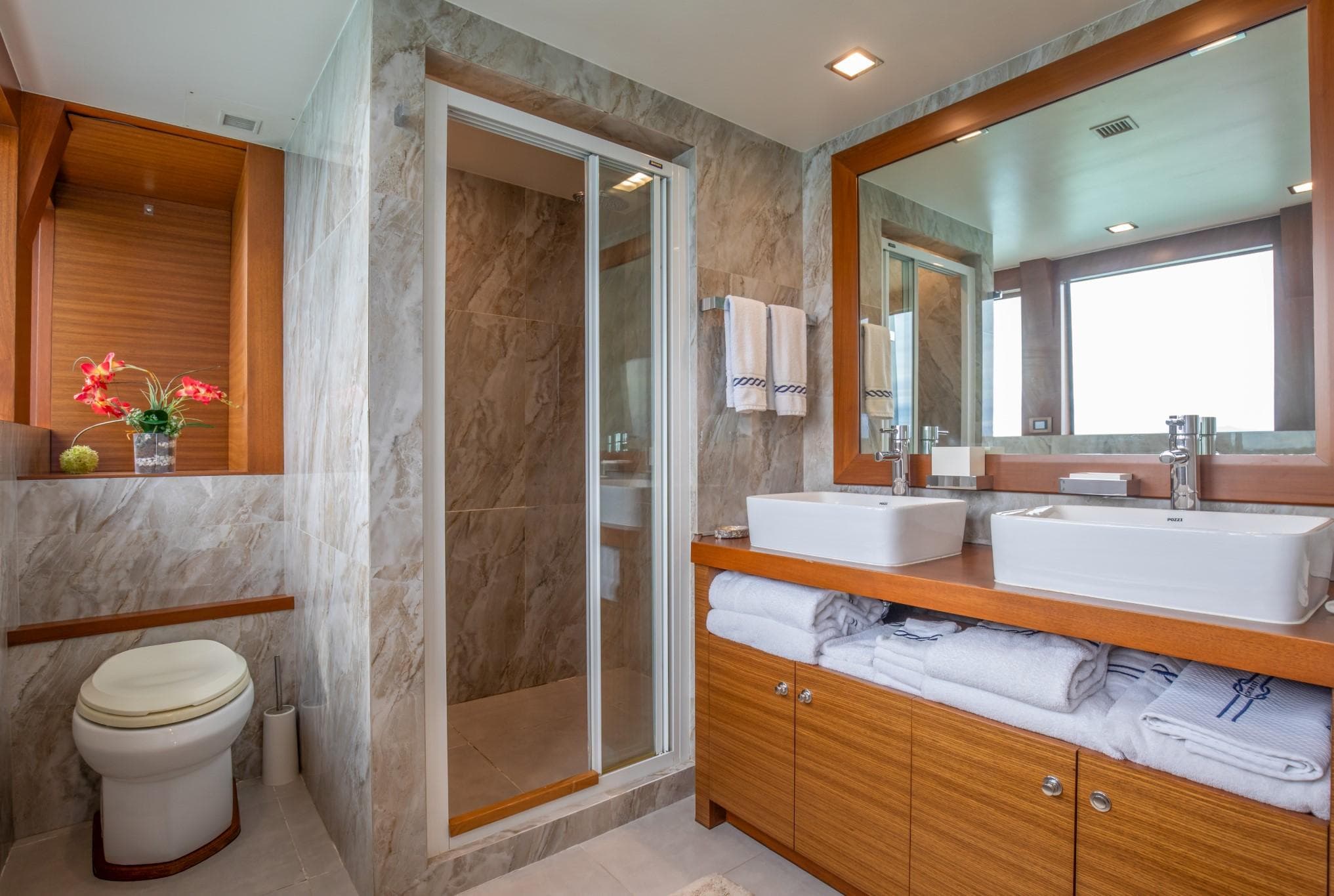 Luxurious bathroom with dual sinks, wooden cabinetry, and a glass shower in a 1992 Custom Niigata.