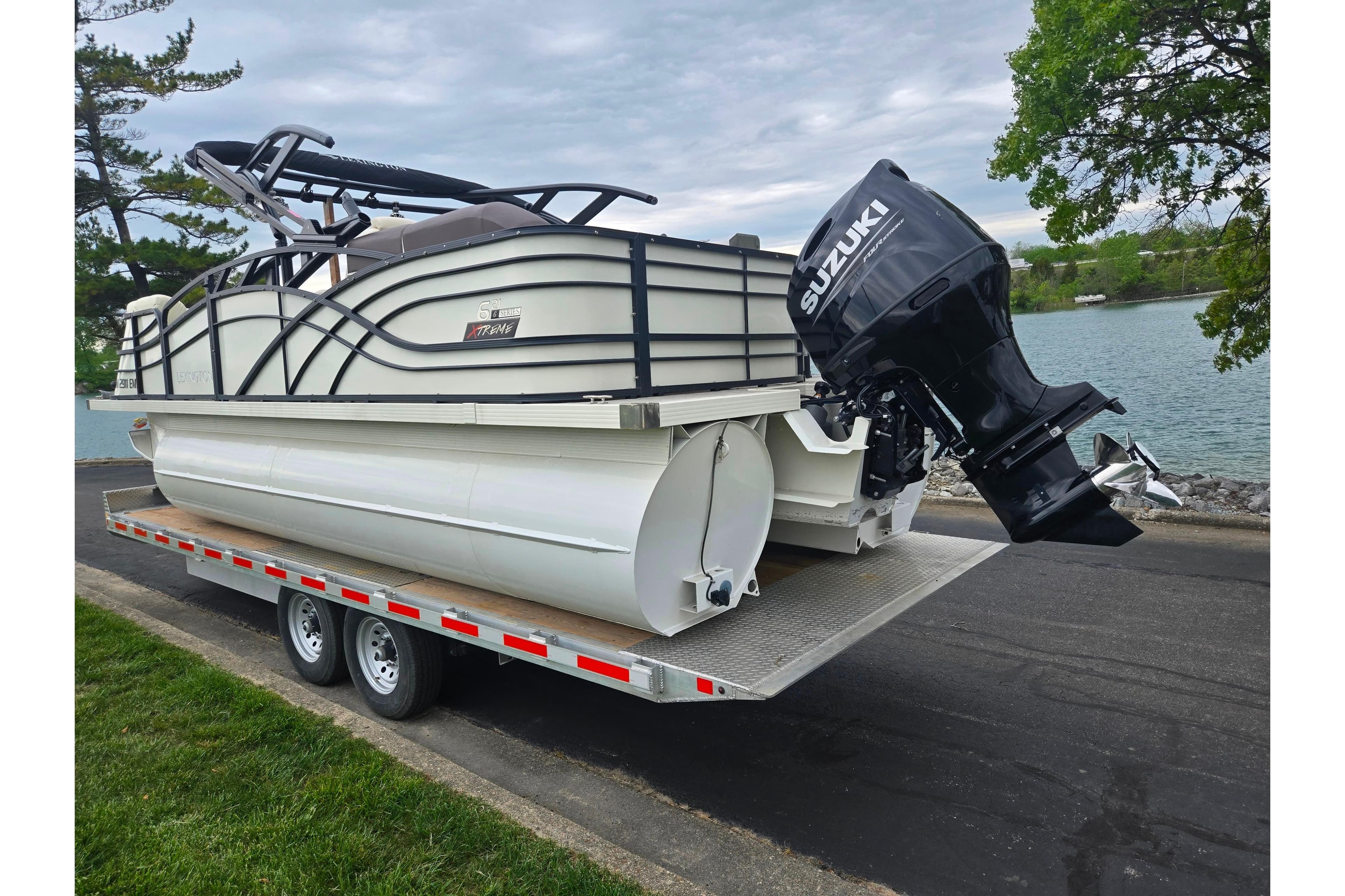 2022 Lexington 621TT Extreme pontoon boat on trailer with Suzuki outboard motor by a lake.