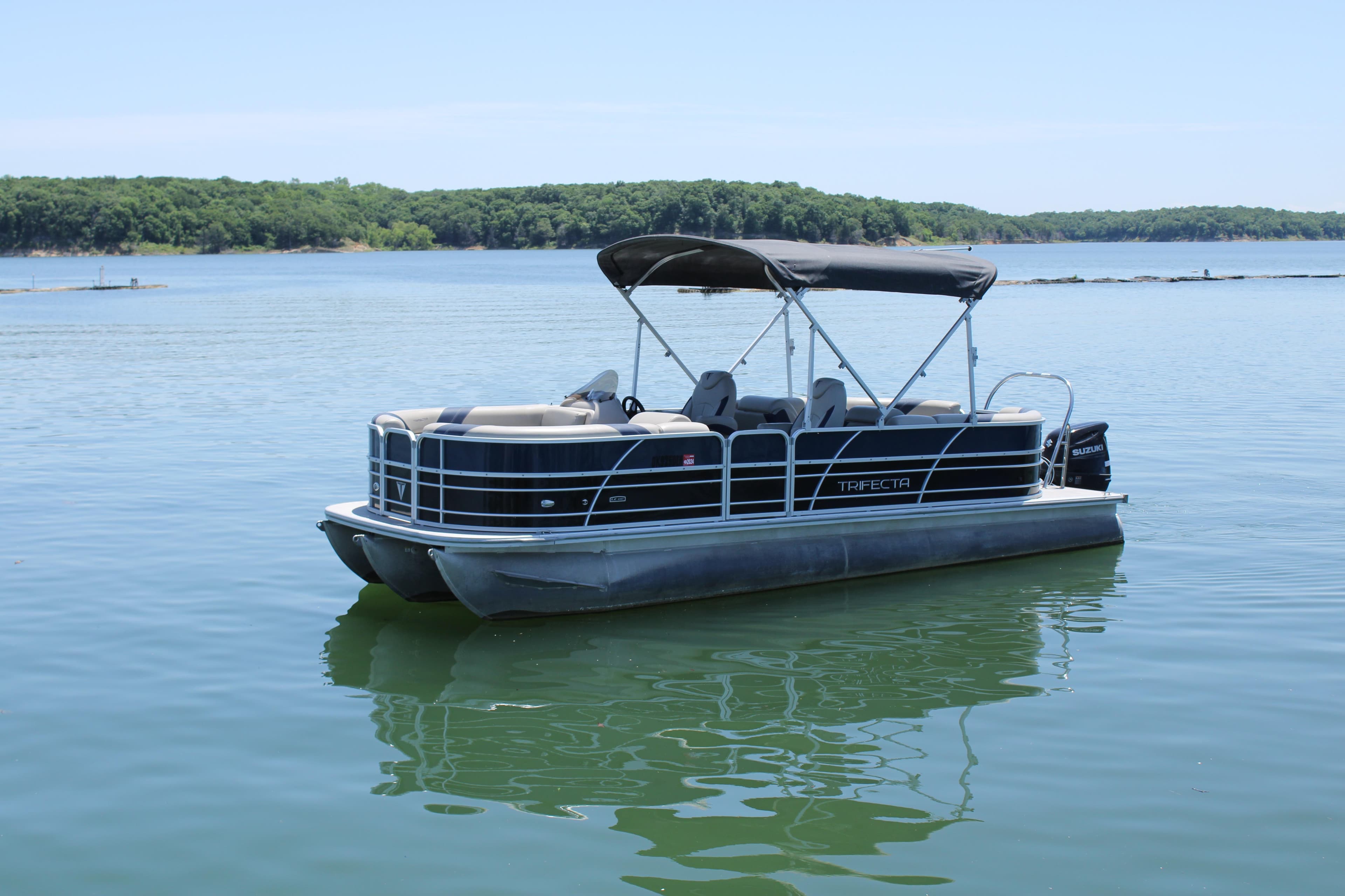 2022 Trifecta RFLE pontoon boat on calm lake with lush green shoreline.