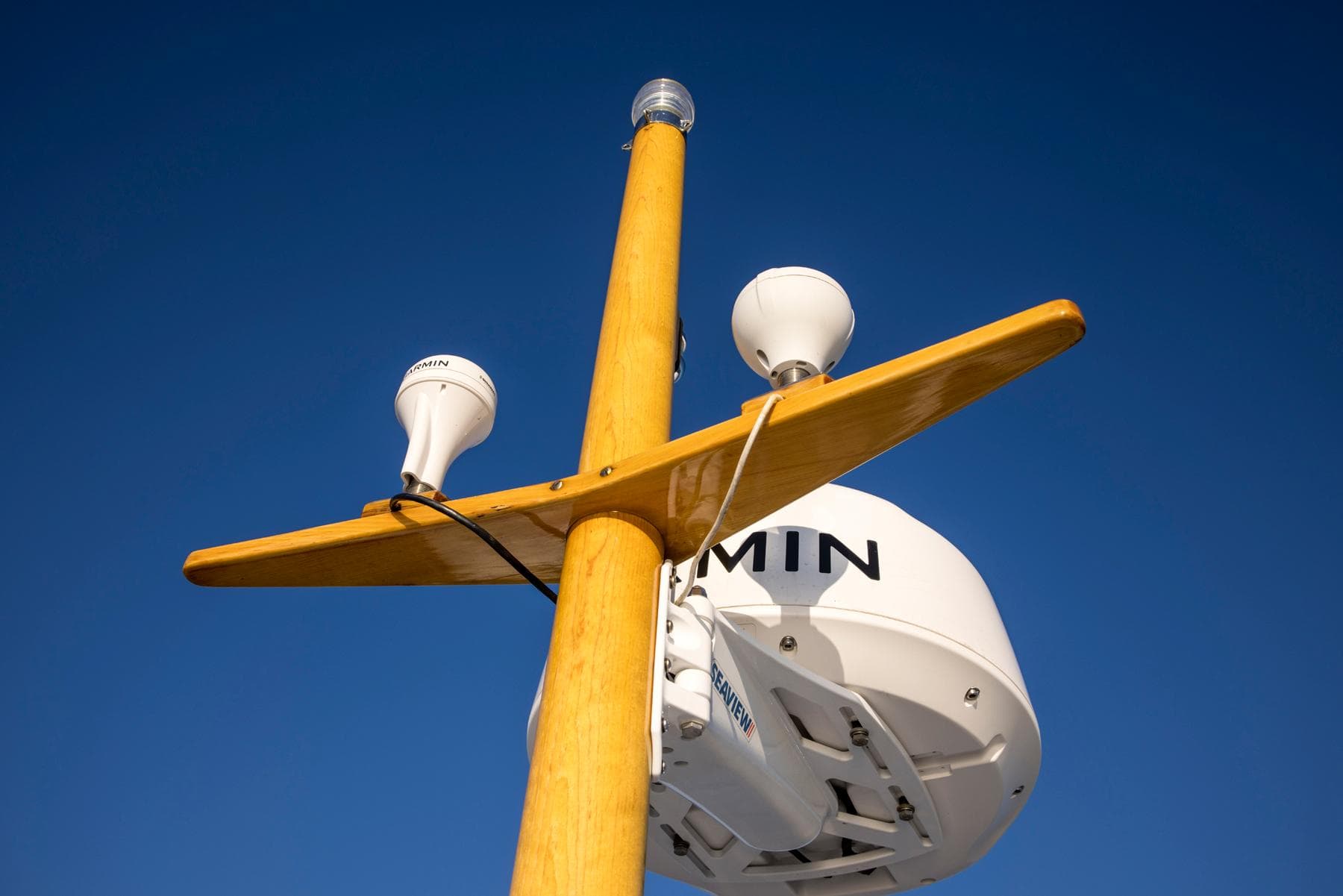 Wooden mast with radar and antennas on 1964 Huckins Out Islander 56 against clear blue sky.