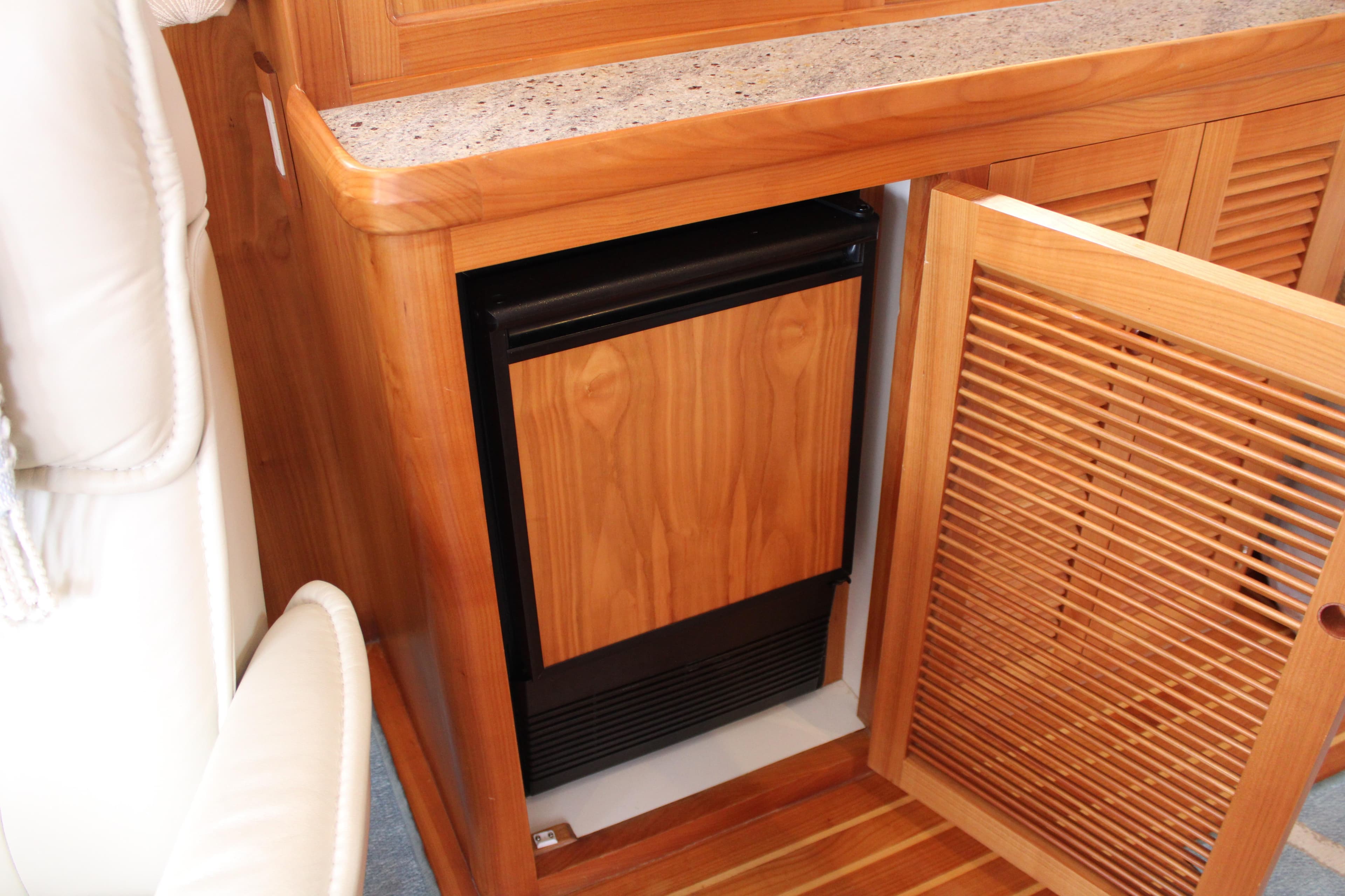 Wooden cabinet with open door revealing a compact refrigerator on a 2023 Krogen Express 52'.