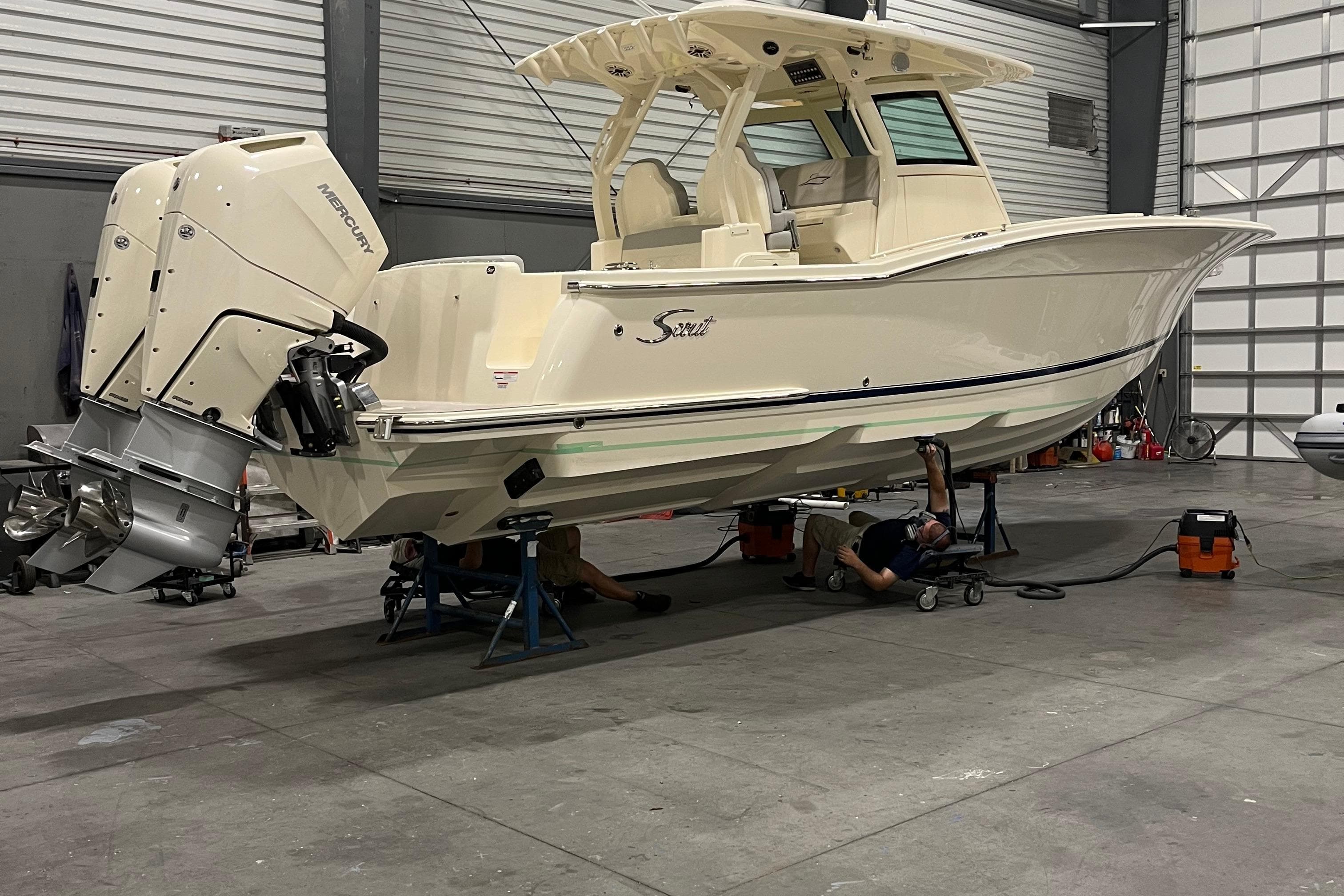 2026 Scout 330 LXF boat in a workshop with dual Mercury outboard engines.