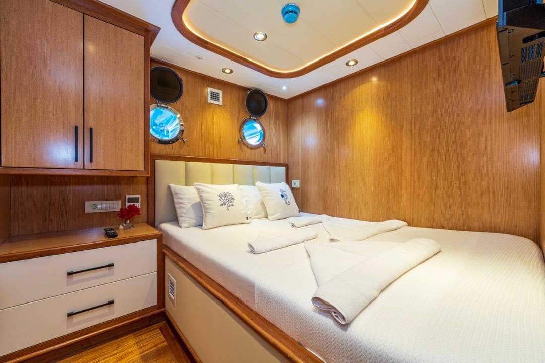Luxurious cabin interior of 2022 Gulet 24 m yacht with wood paneling and cozy bedding.