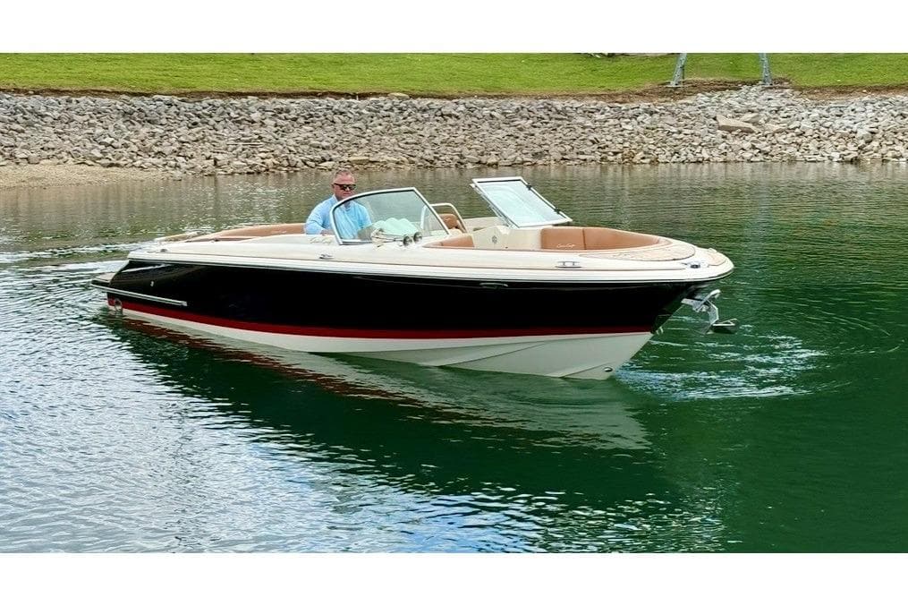 2017 Chris-Craft Launch 25 boat cruising on a calm lake with a rocky shoreline.