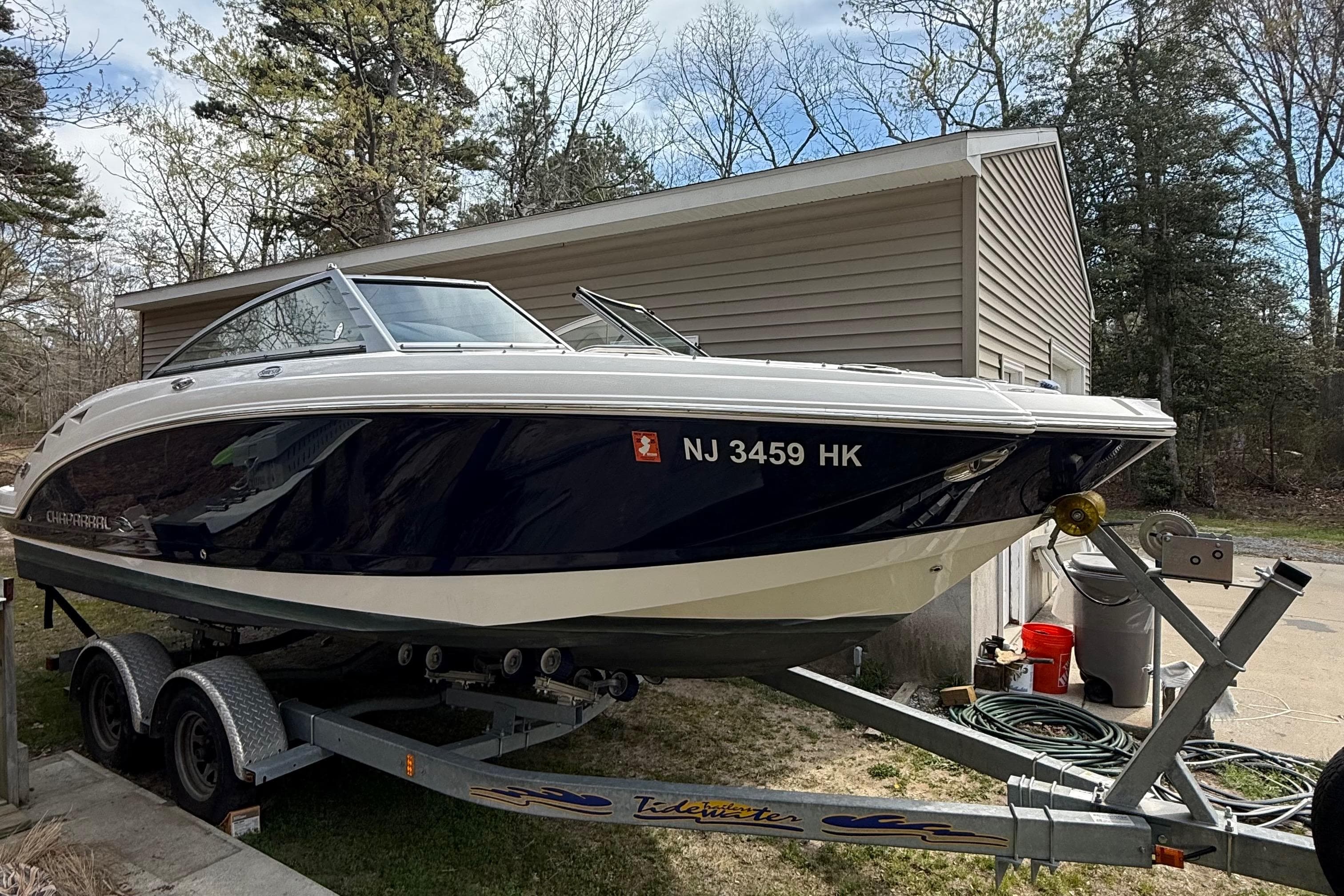 2016 Chaparral 224 Sunesta boat on trailer near garage, surrounded by trees.