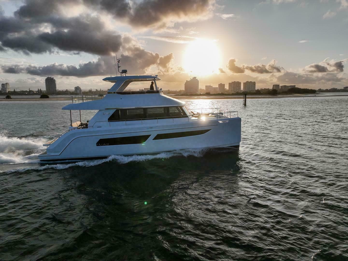 Luxury yacht ILIAD 53F cruising at sunset, 2026 model, with city skyline in background.