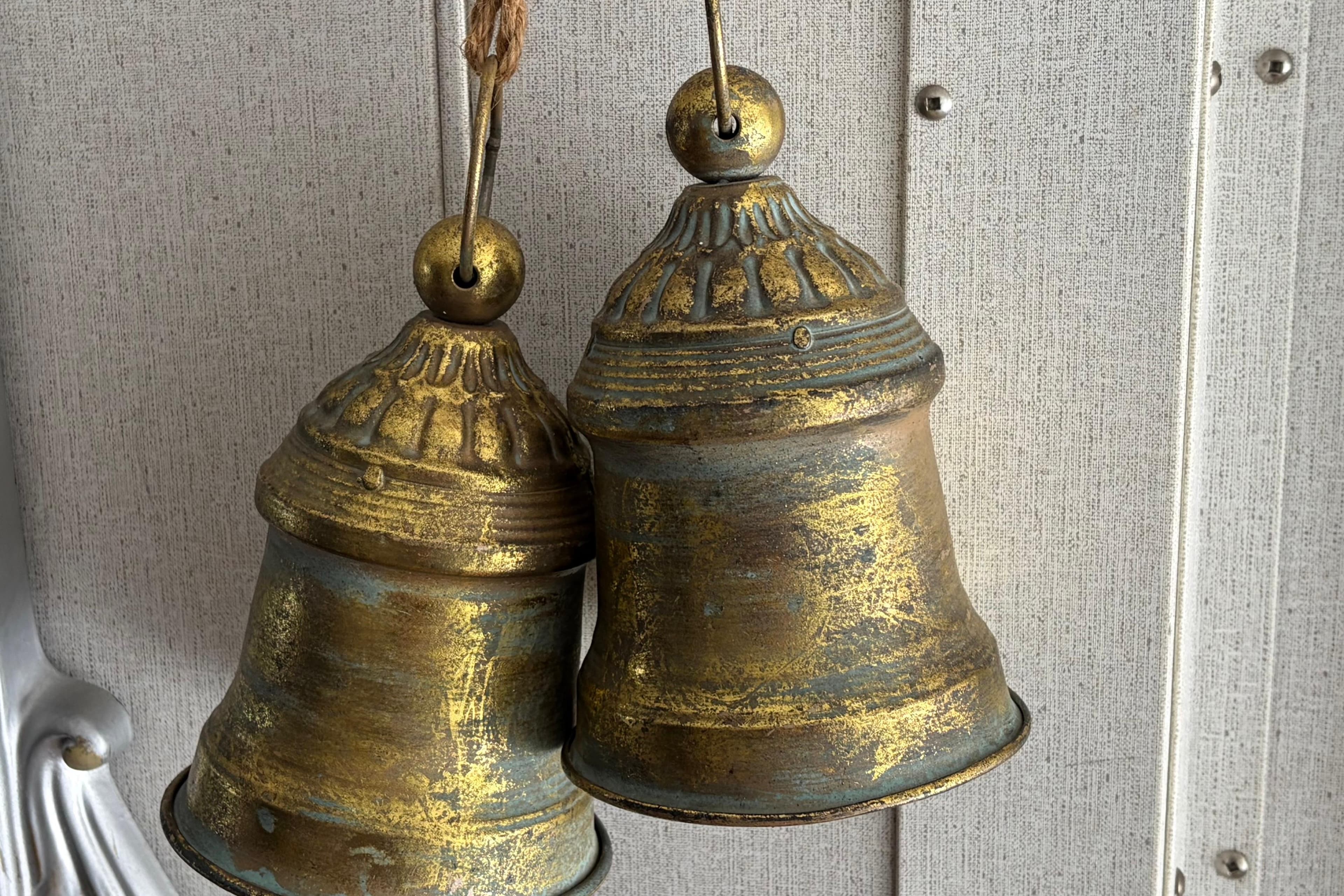 Vintage brass bells hanging on a textured wall, showcasing rustic charm.