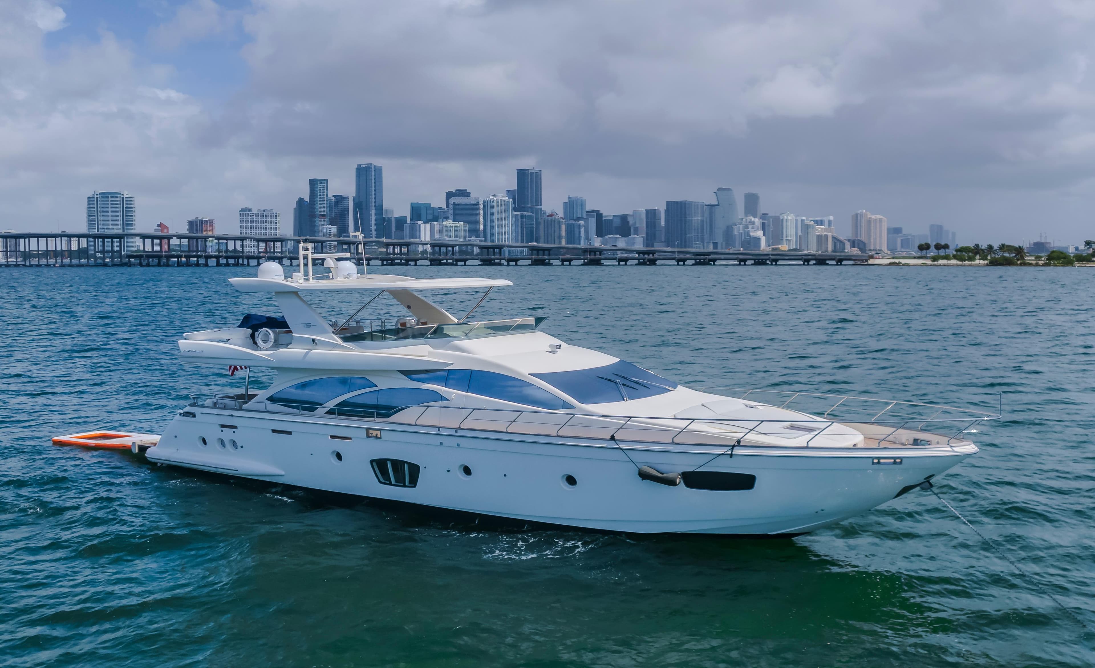2008 Azimut Flybridge yacht cruising near city skyline on a cloudy day.