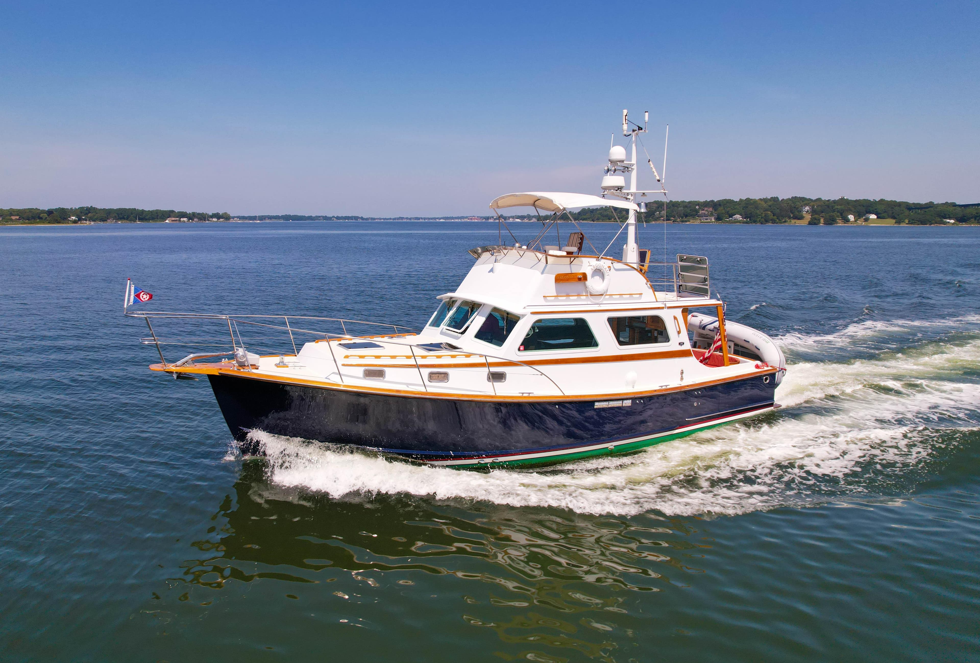 1984 Wilbur 38 yacht cruising on a calm lake under a clear blue sky.