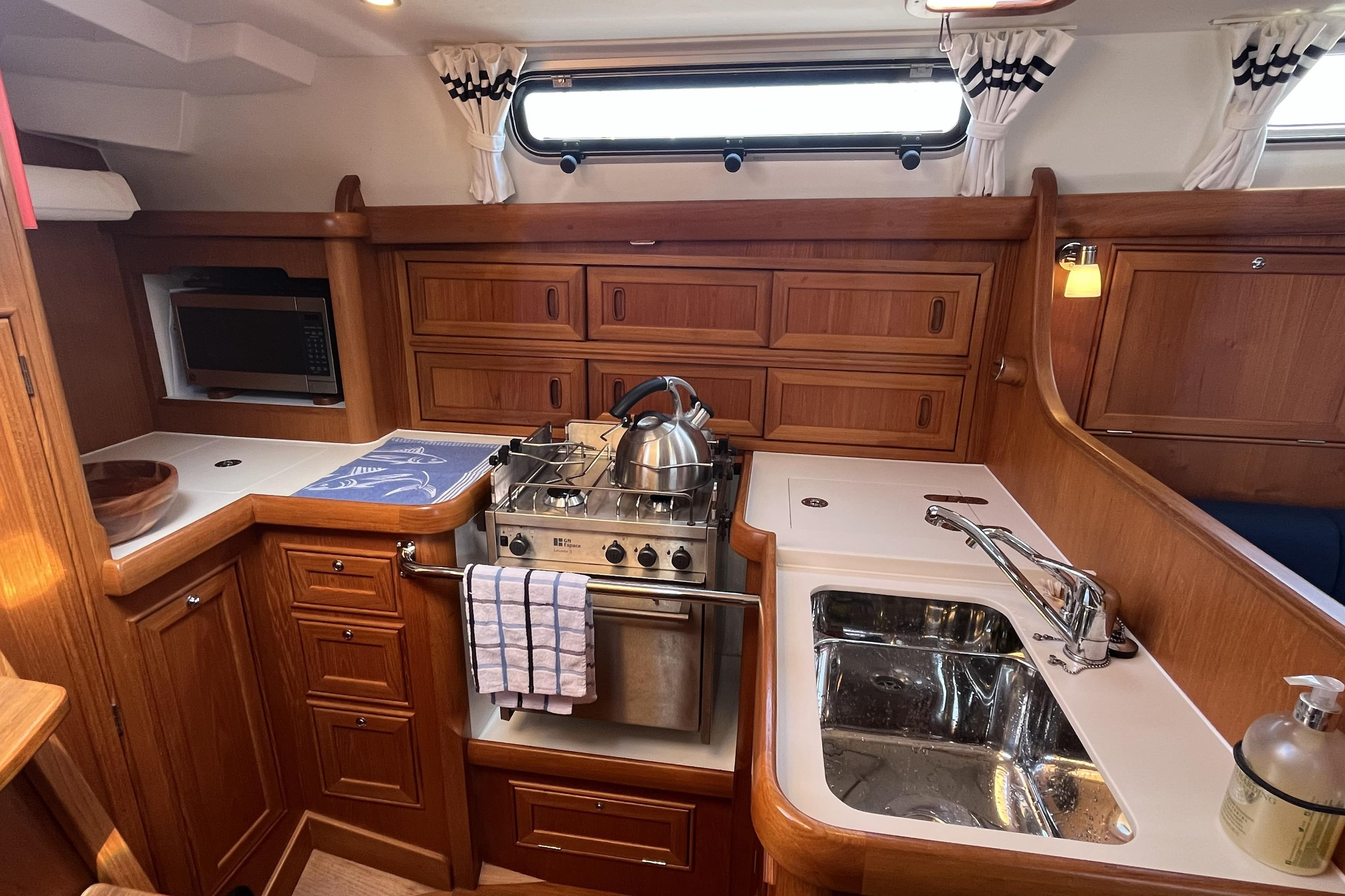 2017 Rustler 37 yacht kitchen with wooden cabinetry, stove, sink, and microwave.