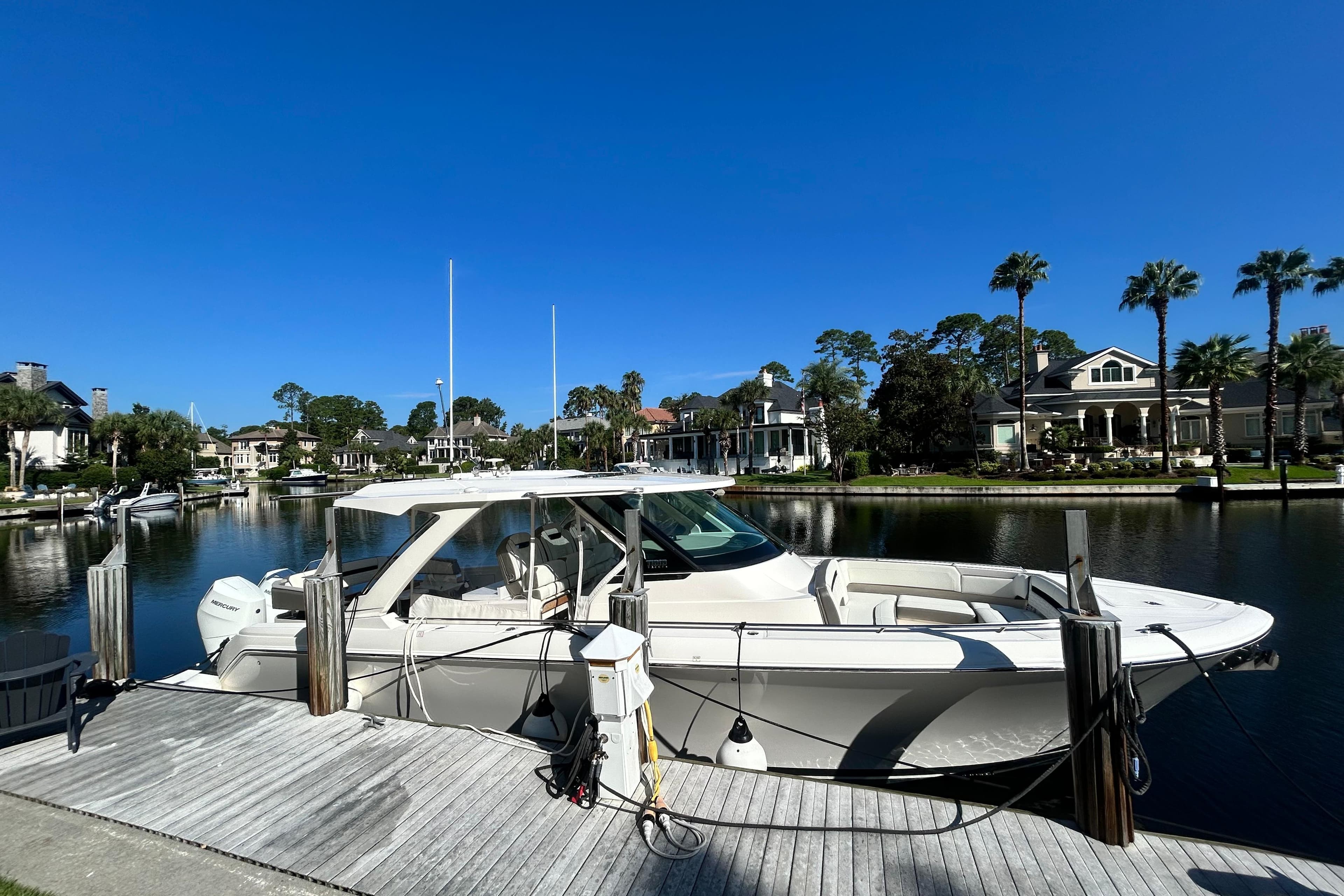2023 Tiara Yachts 38 LS docked by waterfront homes under clear blue sky.