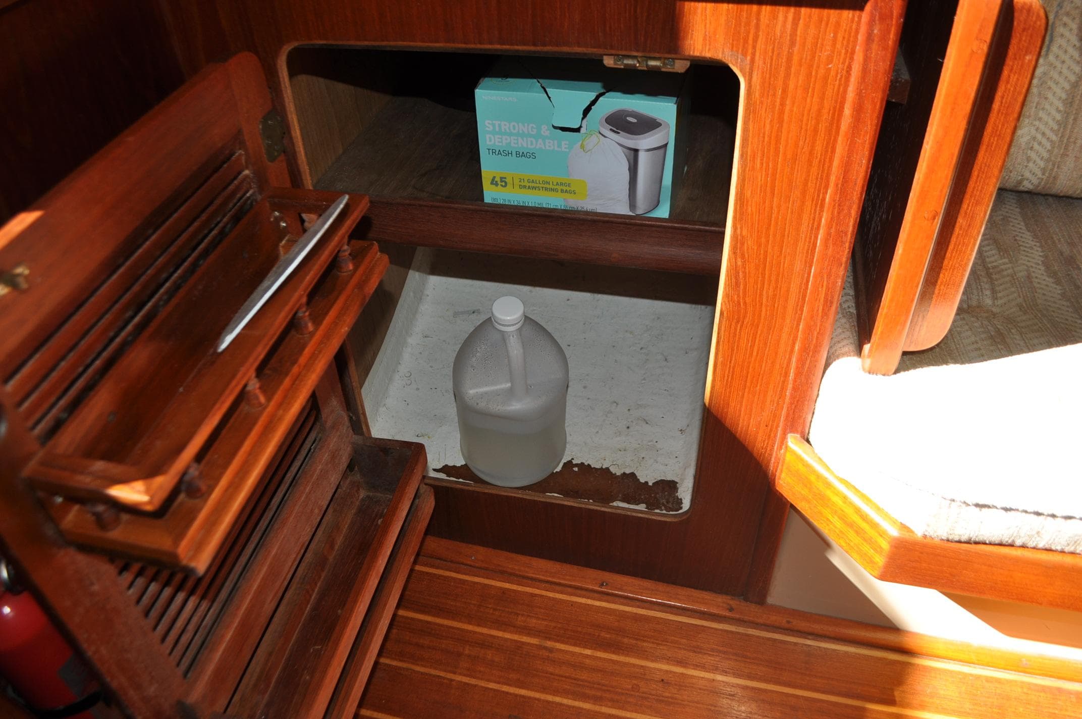 1989 Island Packet 27 interior storage with cleaning supplies and wooden cabinetry.