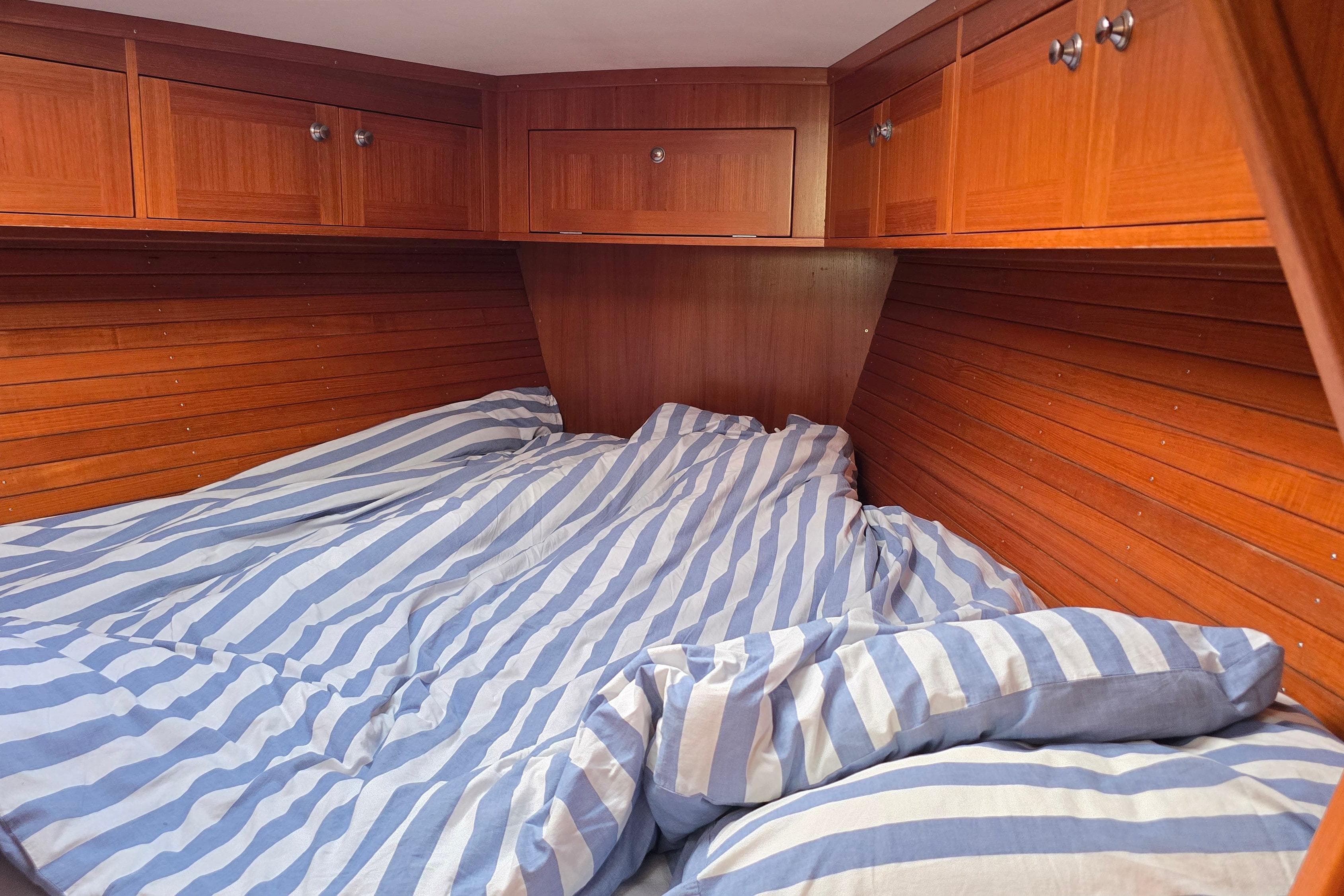 Cozy cabin interior of 2002 Comfortina 42 yacht with striped bedding and wooden cabinets.