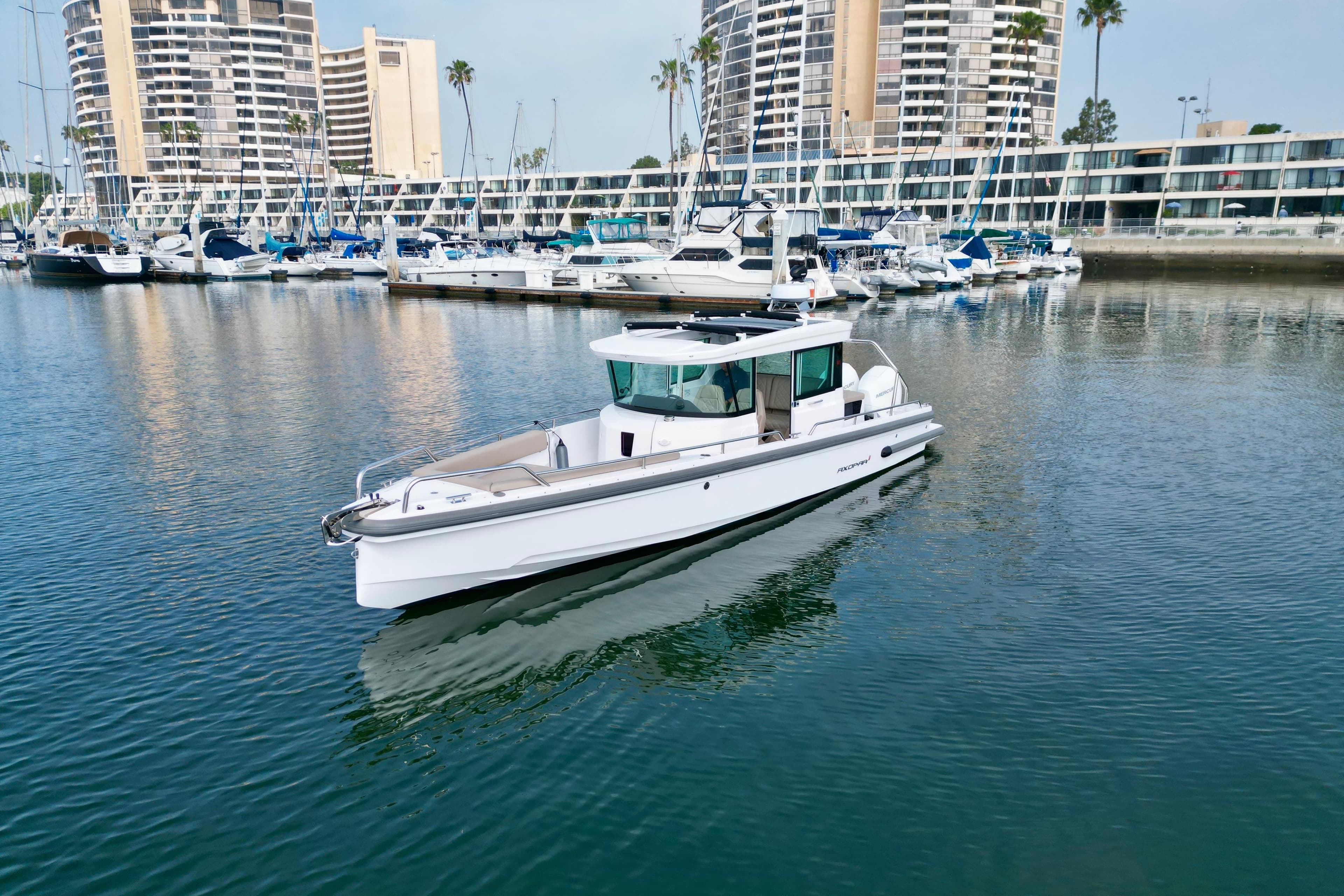 2023 Axopar 28 Cabin boat in marina with modern buildings in background.