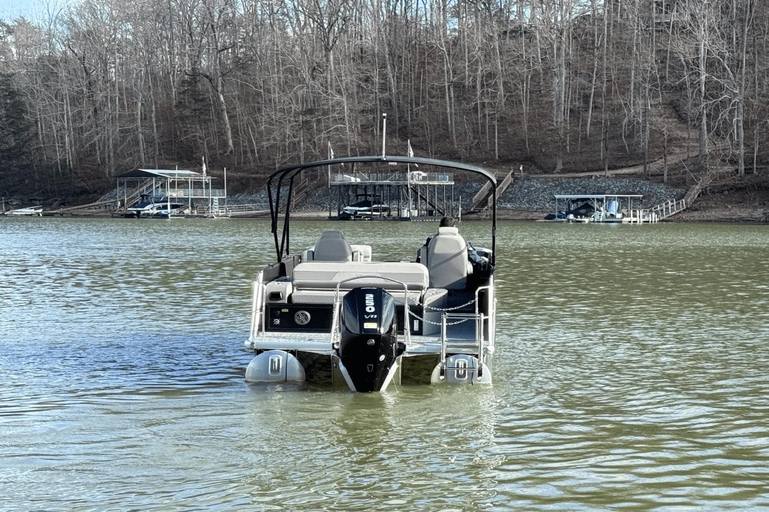 2024 Premier 230 Solaris pontoon boat on a lake with wooded shoreline.