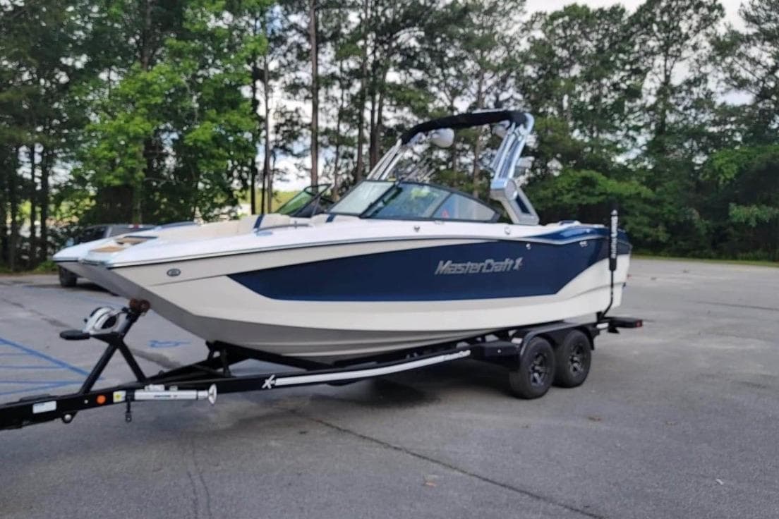 2022 MasterCraft X24 boat on trailer in parking lot, surrounded by trees.