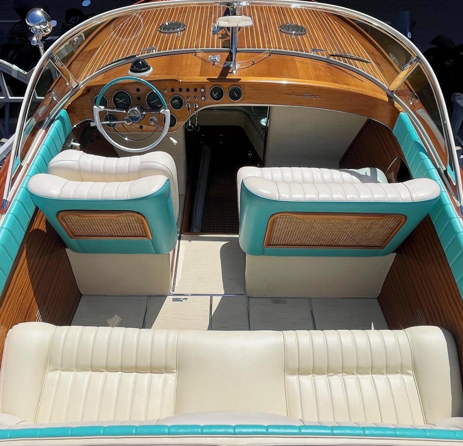 1974 Riva Aquarama Special boat interior with turquoise and cream seating, wooden dashboard, and steering wheel.