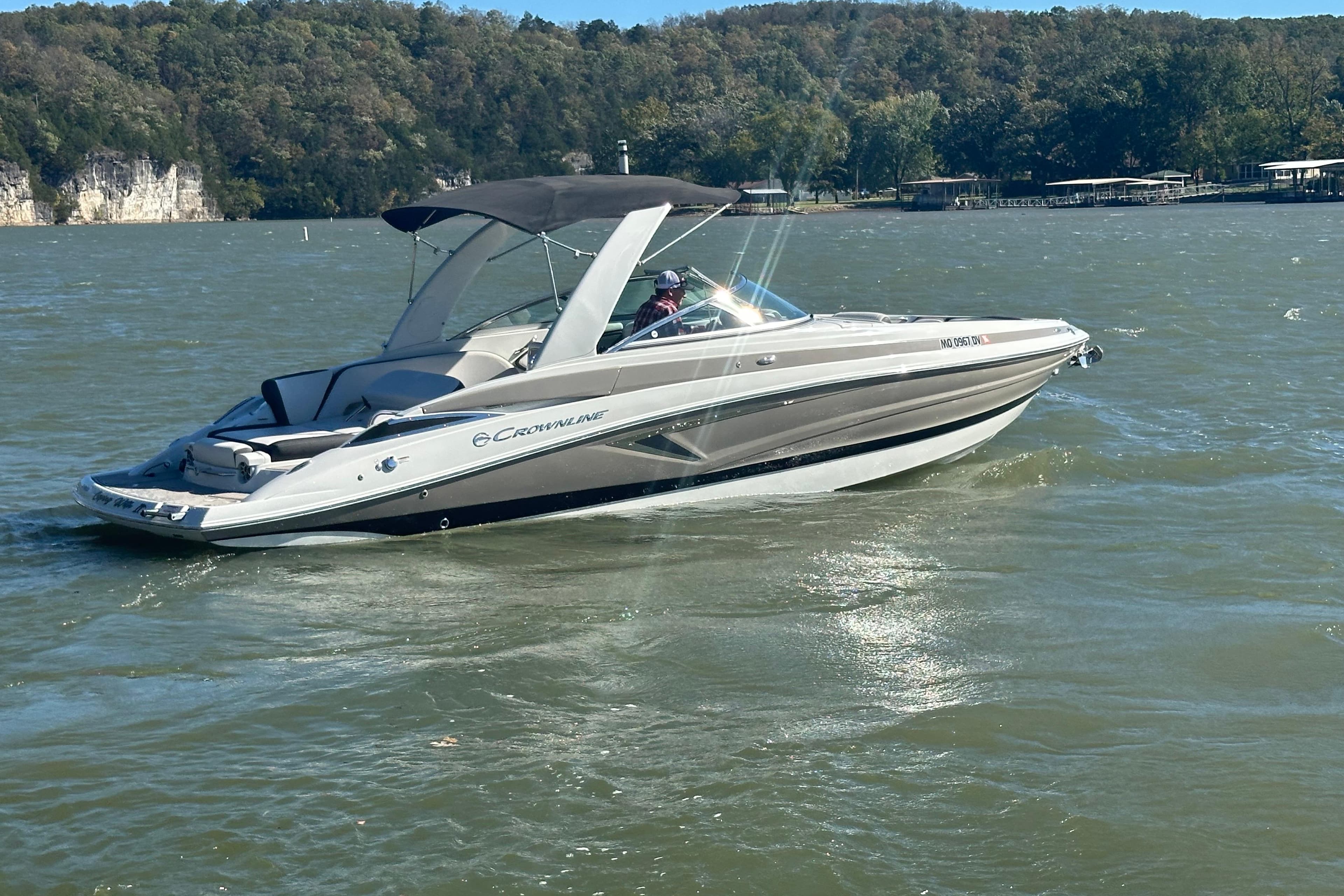 2023 Crownline 290 CR boat cruising on a scenic lake with forested shoreline.