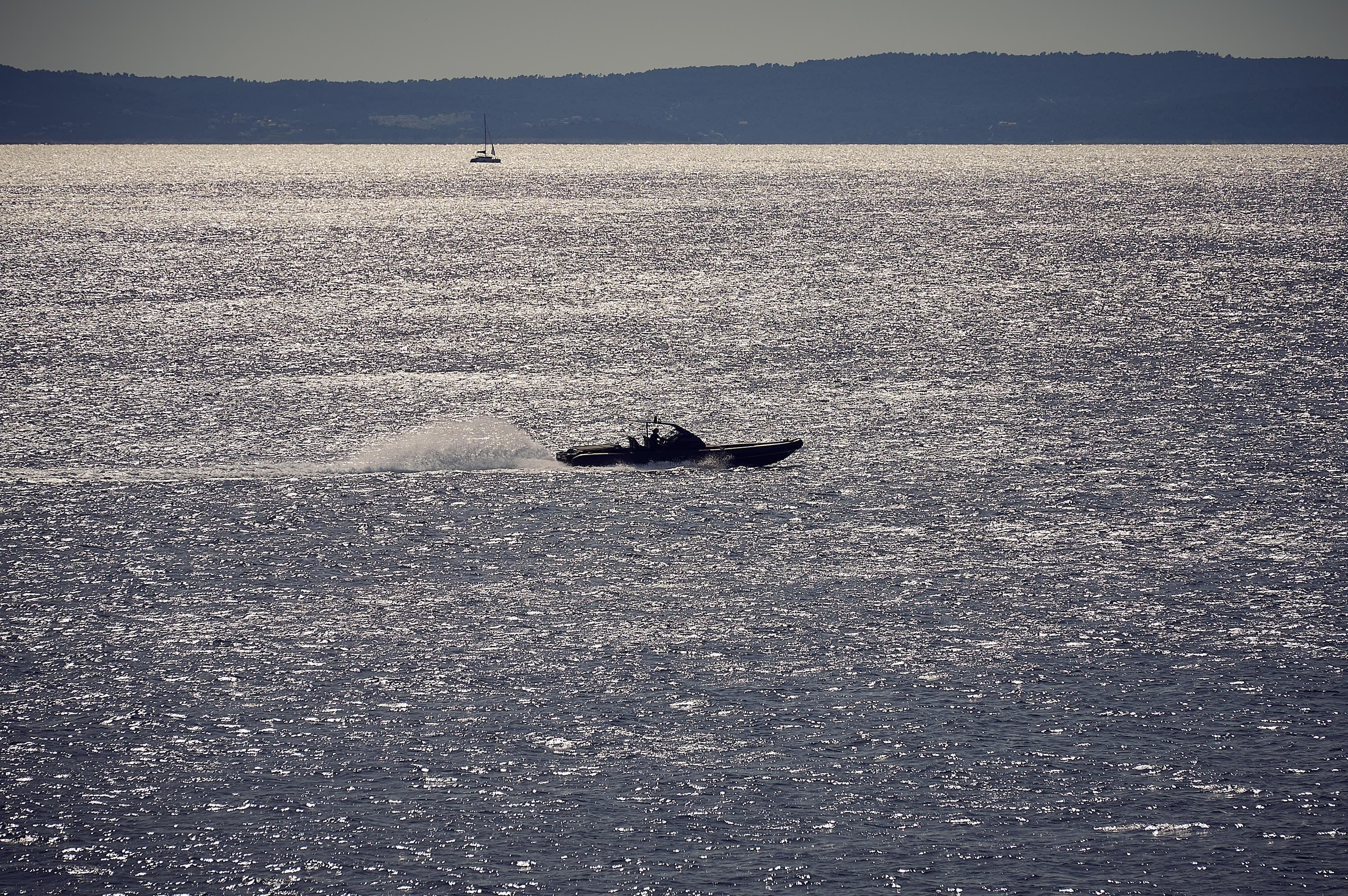 2016 Goldfish 38 Supersport boat speeding on shimmering water with distant sailboat.