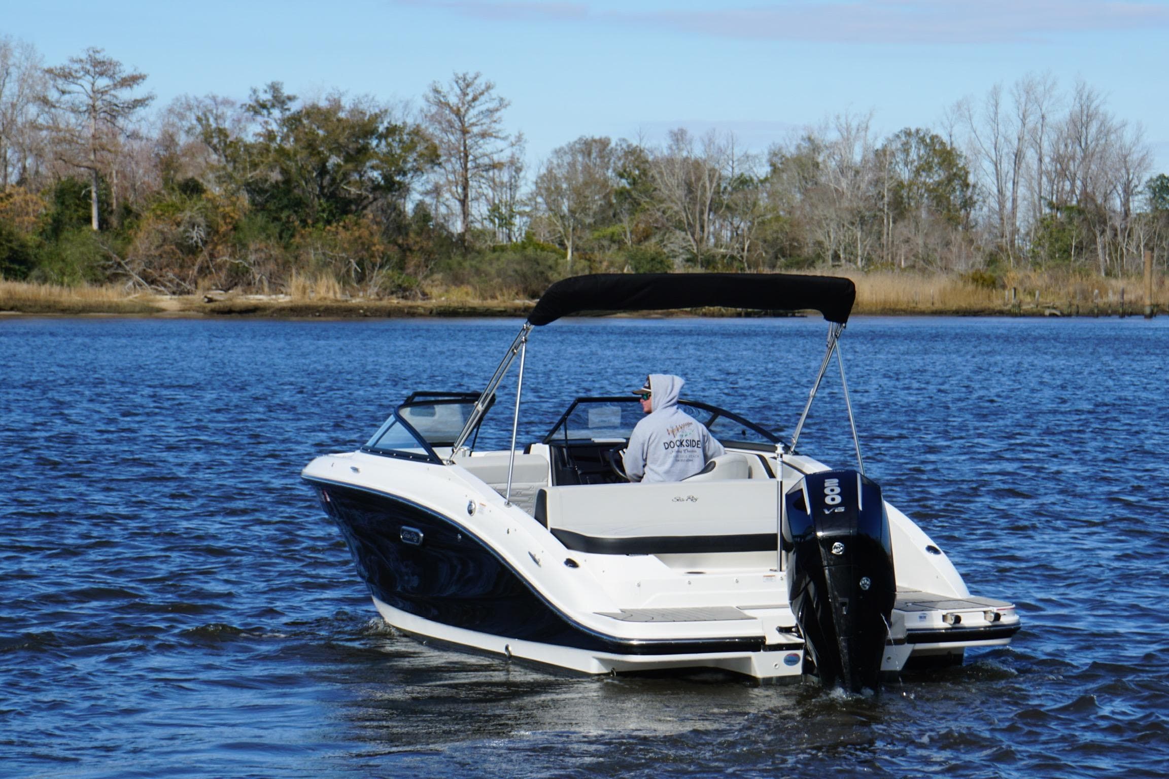 2025 Searay SPX210 boat cruising on a serene lake with trees in the background.