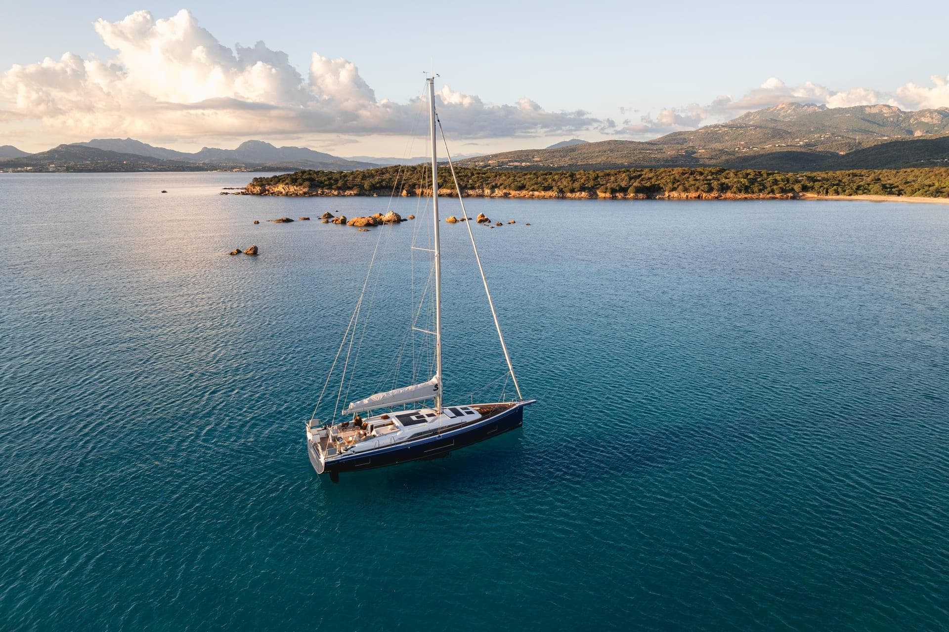 Sailing yacht Beneteau Oceanis 47 (2025) on tranquil blue waters, scenic coastal backdrop.