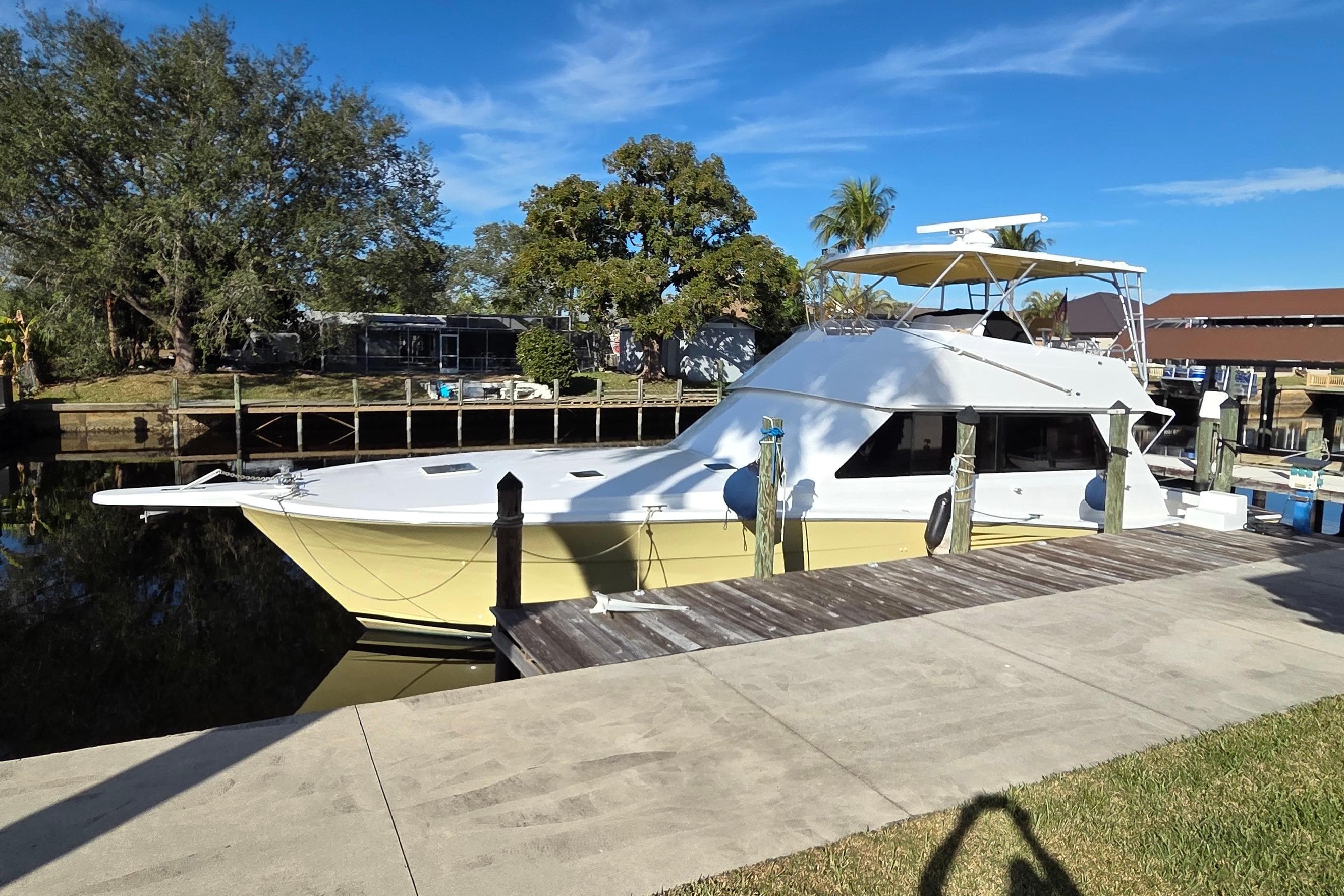 1990 Viking 53 Convertible yacht docked by a wooden pier, surrounded by trees.