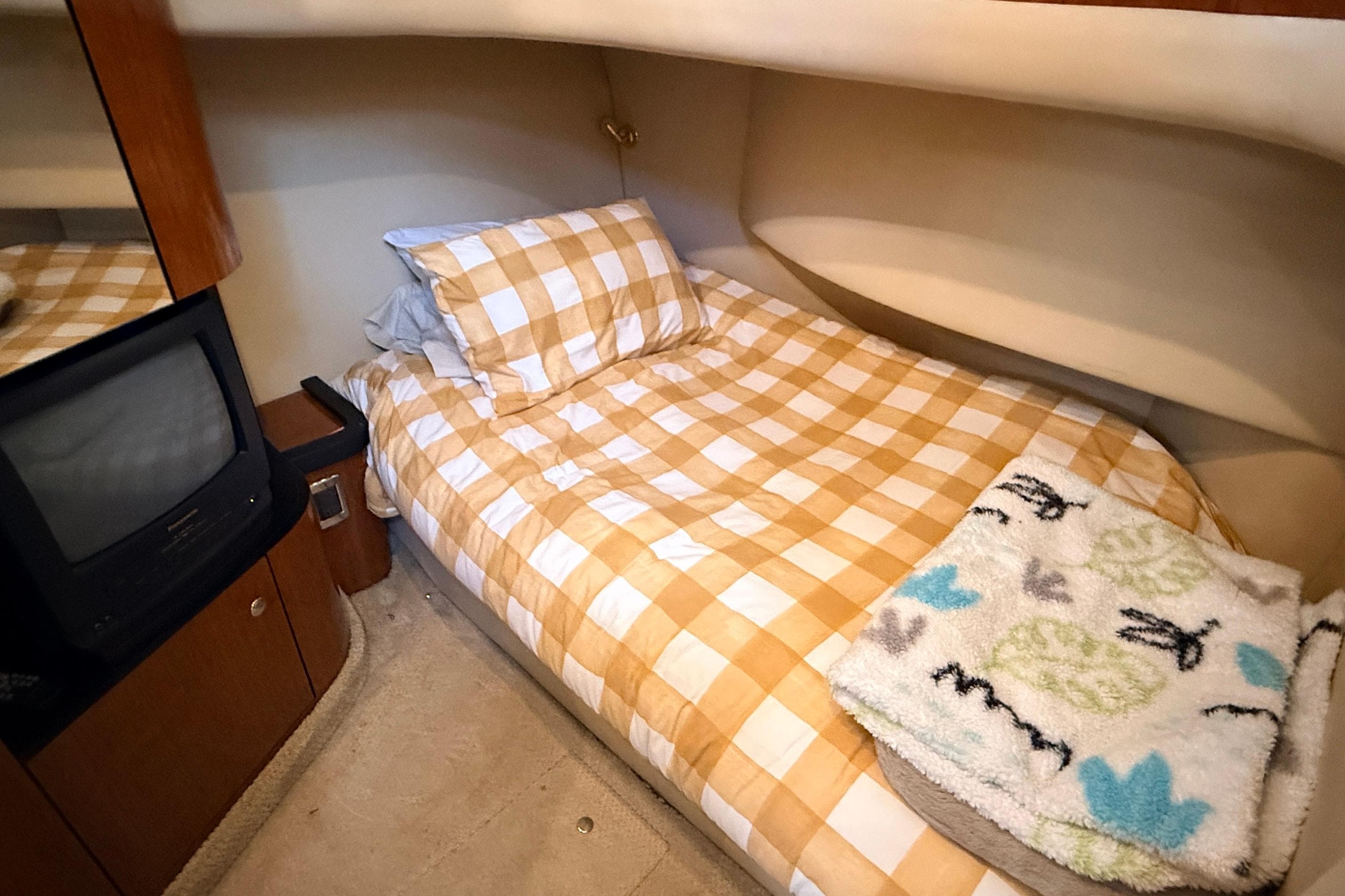 Cozy cabin interior of 2003 Sea Ray 450 Express Bridge with checkered bedding and TV.
