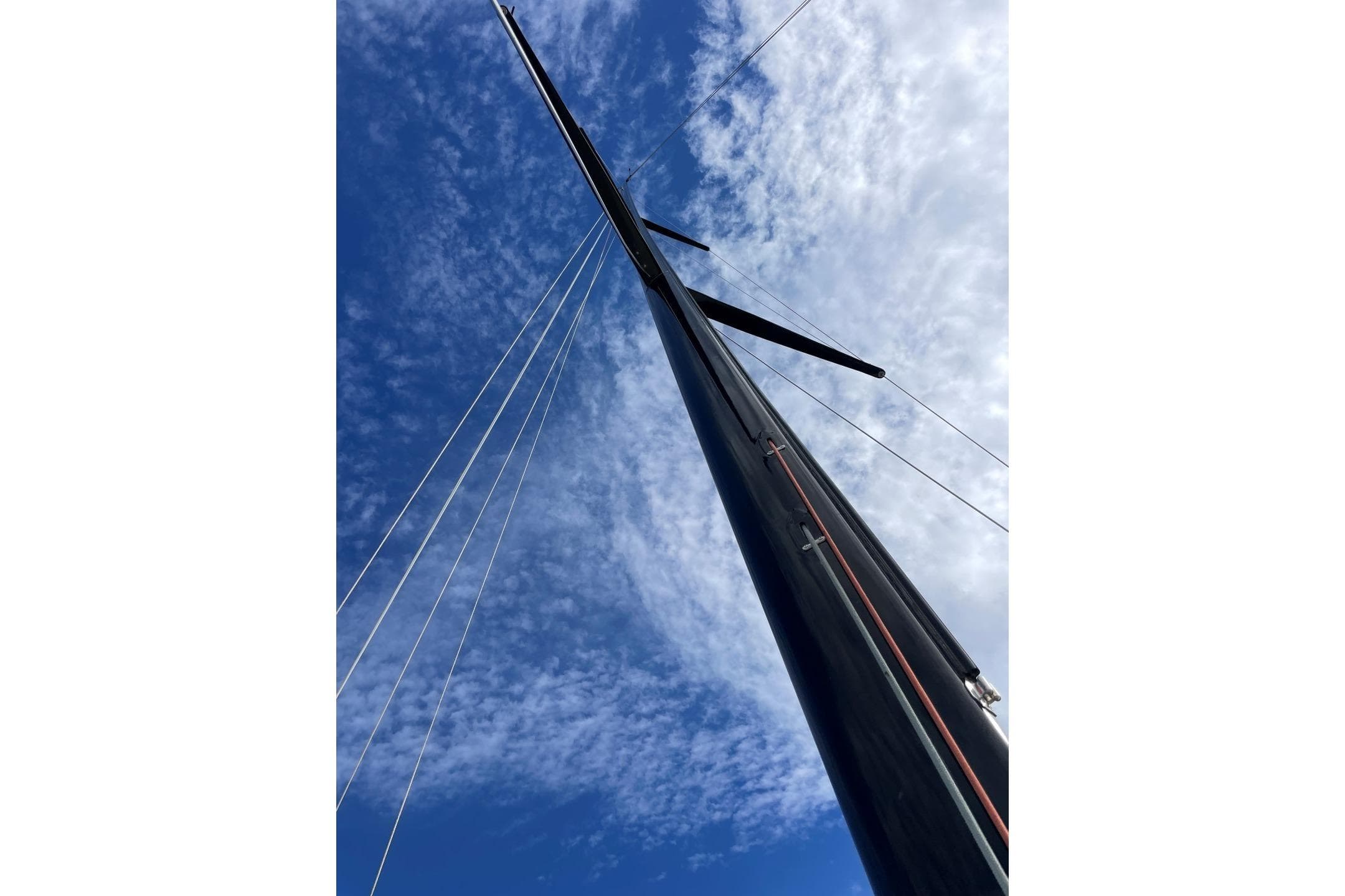 Tall mast of 2005 Botin TP52 sailboat against a blue sky.