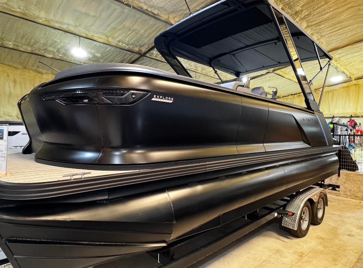 2025 Manitou Explore pontoon boat in a showroom, featuring sleek black design.