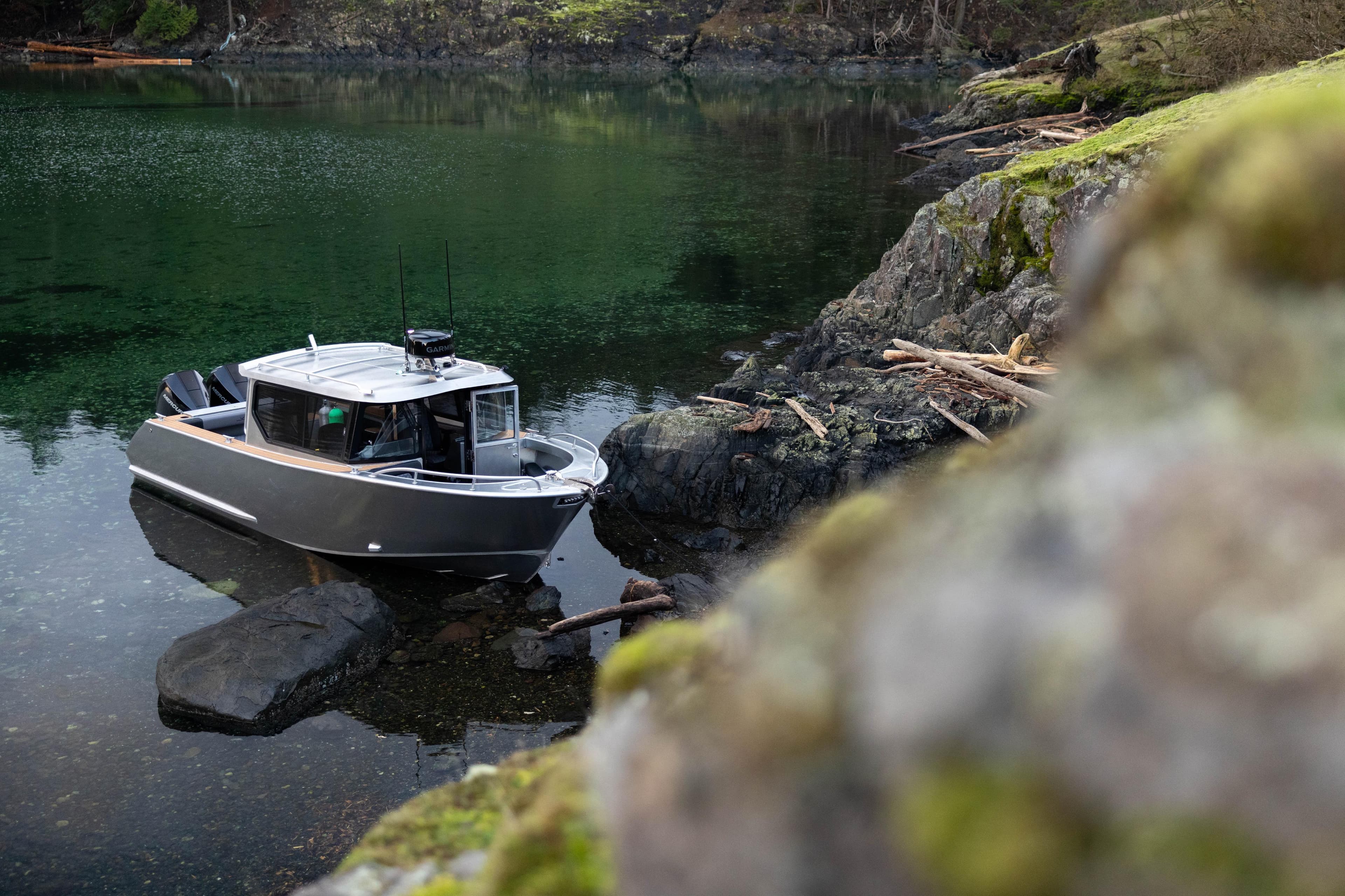 Jasper Marine Defender 22 boat, 2026 model, docked by rocky shoreline in serene waters.