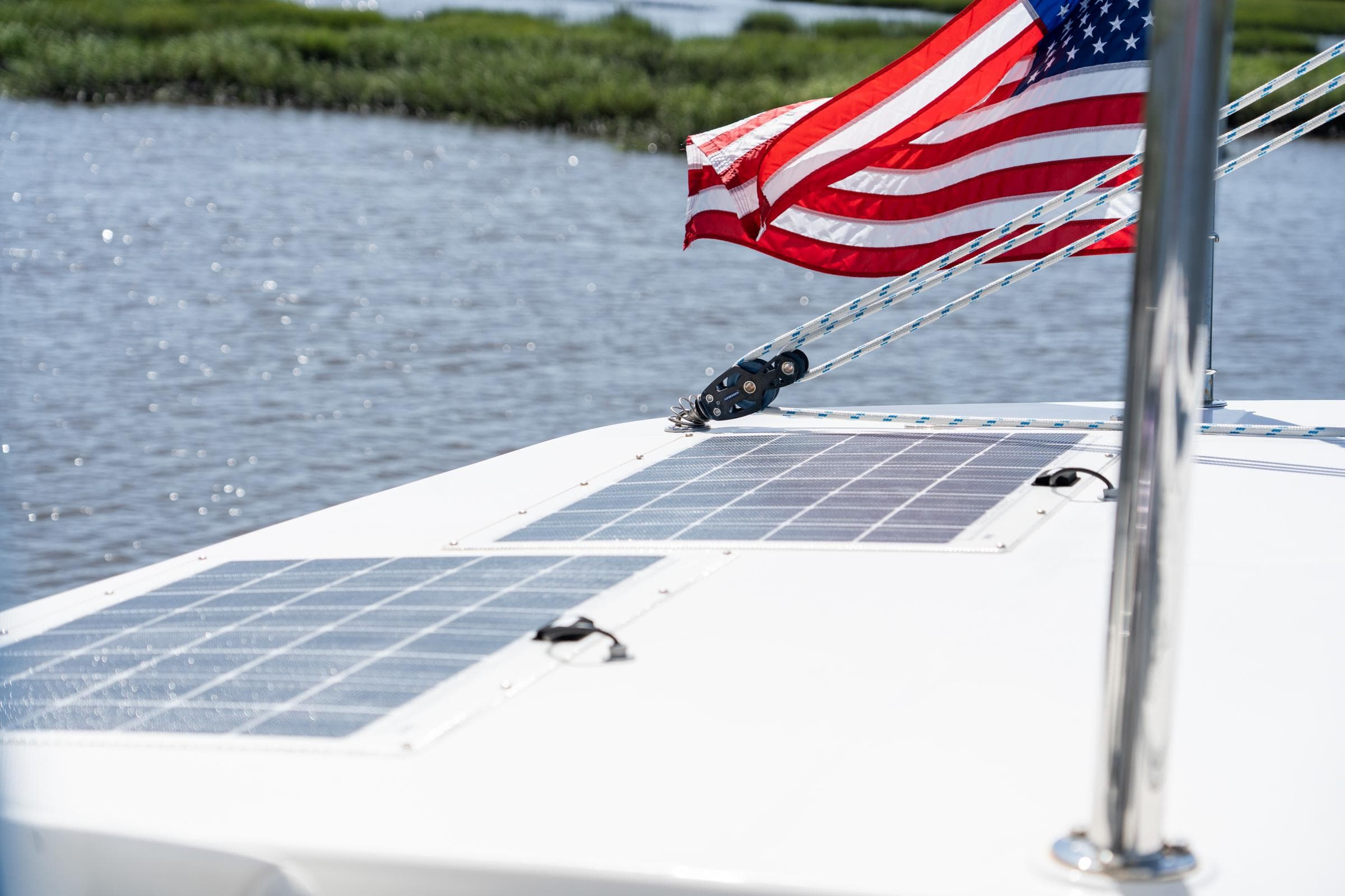 Solar panels on 2016 Leopard 44 catamaran with American flag, near water and greenery.