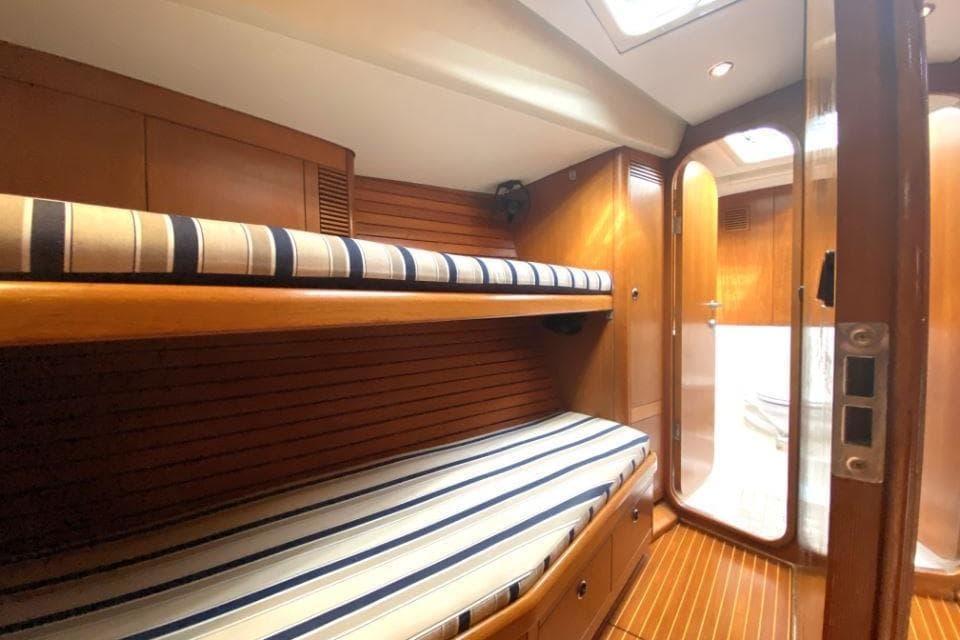 Interior of 1996 Nautor Swan 48 yacht with wooden bunk beds and striped cushions.