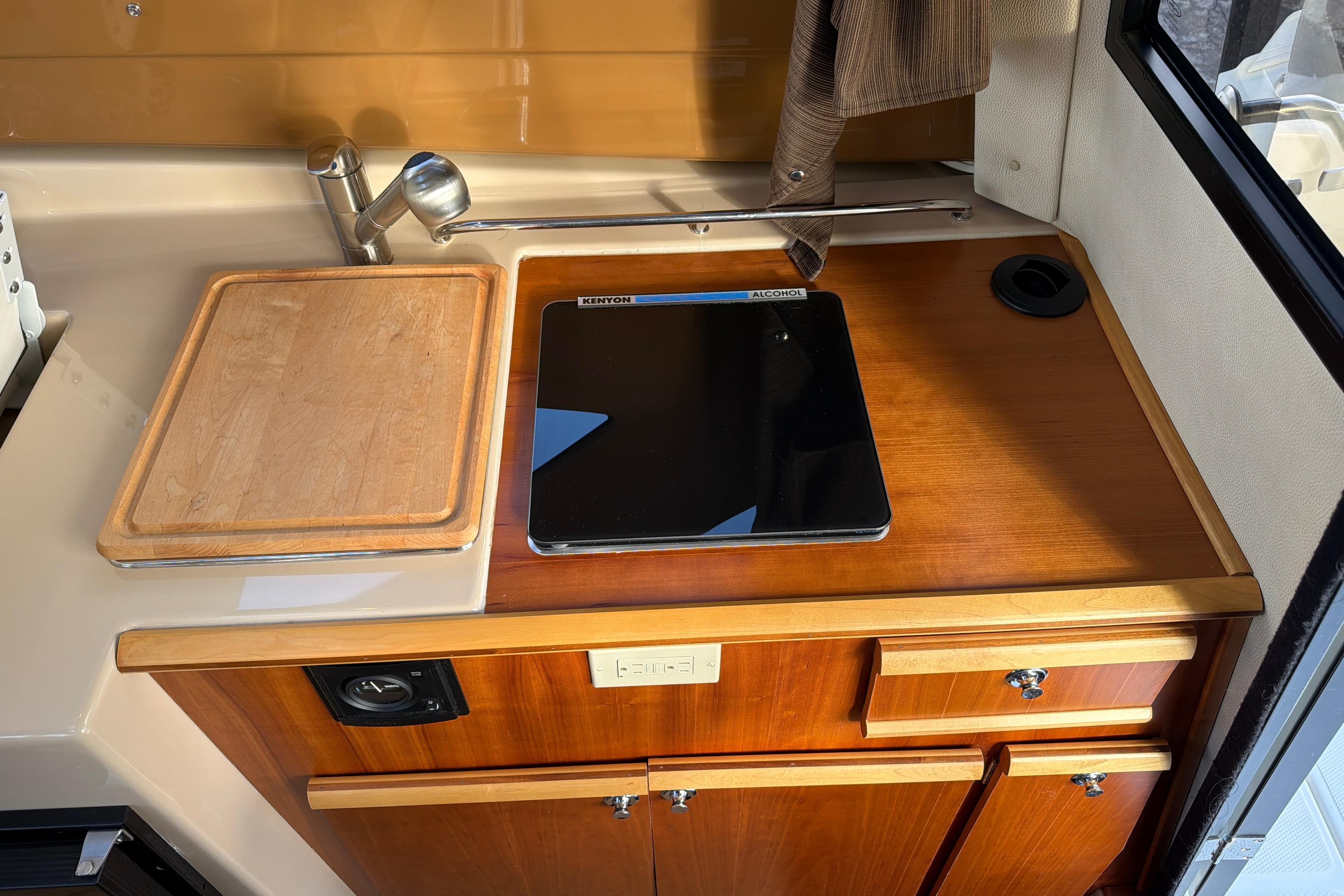 Compact kitchen area in a 2016 Cutwater C-242 Coupe boat with stove and cutting board.
