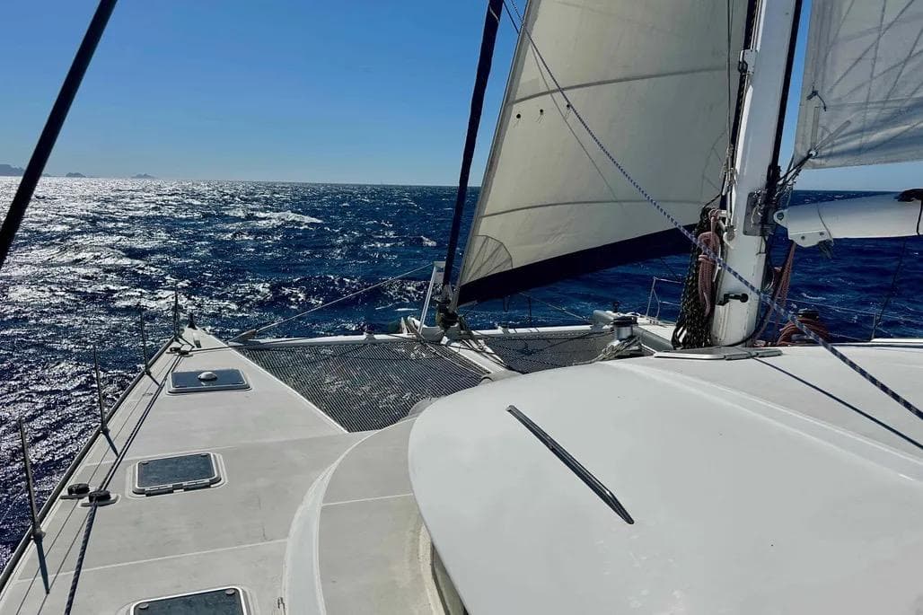 Sailing on a 2002 Lagoon 570 catamaran in open sea under clear blue skies.