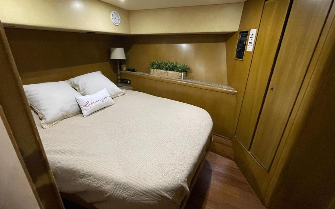 Cozy bedroom in a 1995 Bertram Convertible yacht with wooden interior and double bed.