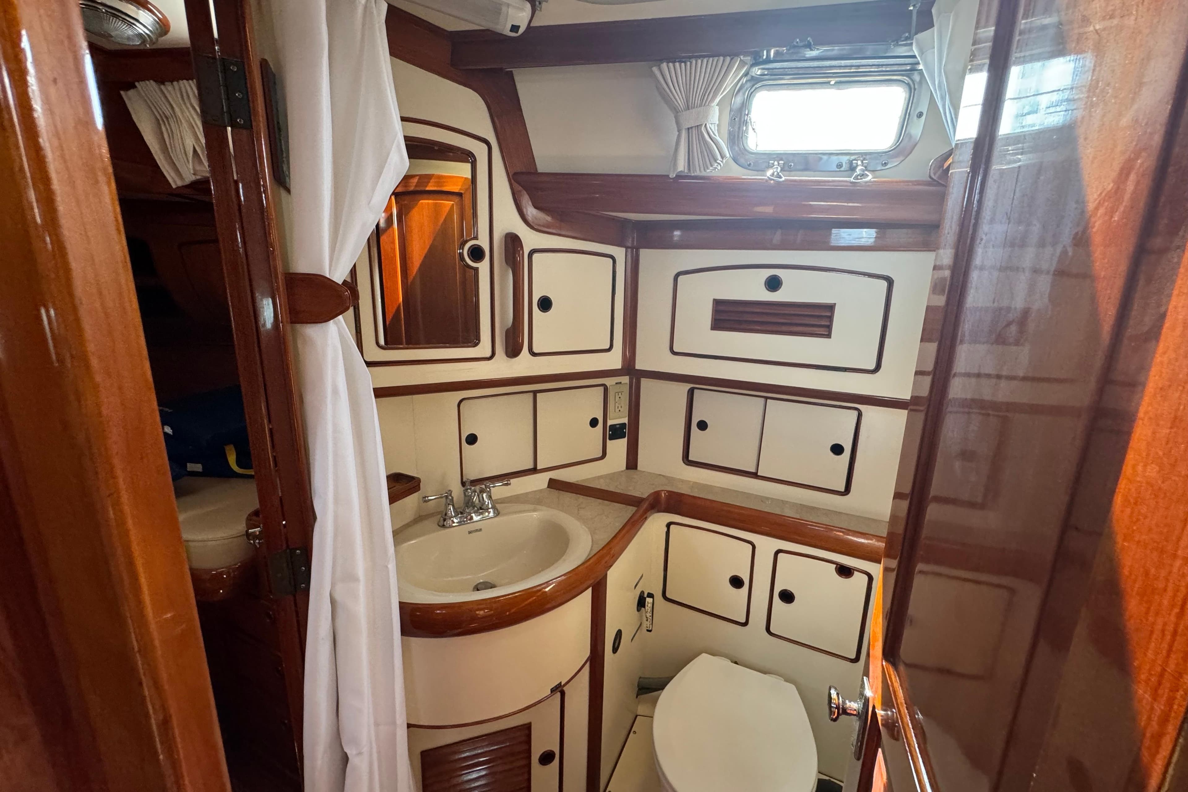1986 Little Harbor 46 Center Cockpit yacht bathroom with wooden cabinetry and porthole window.