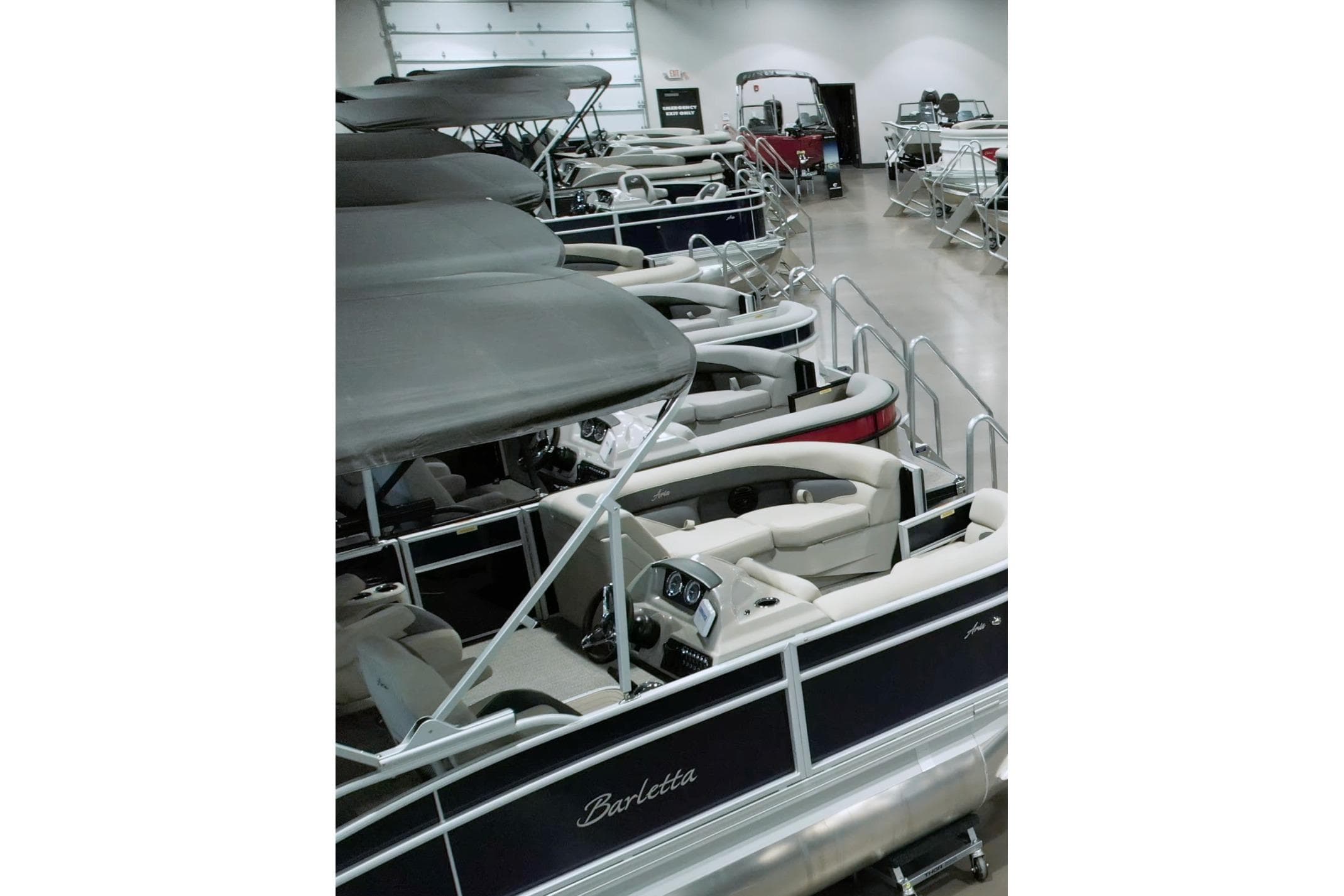 Indoor showroom displaying multiple pontoon boats, including a 2026 Xpress H18 model.