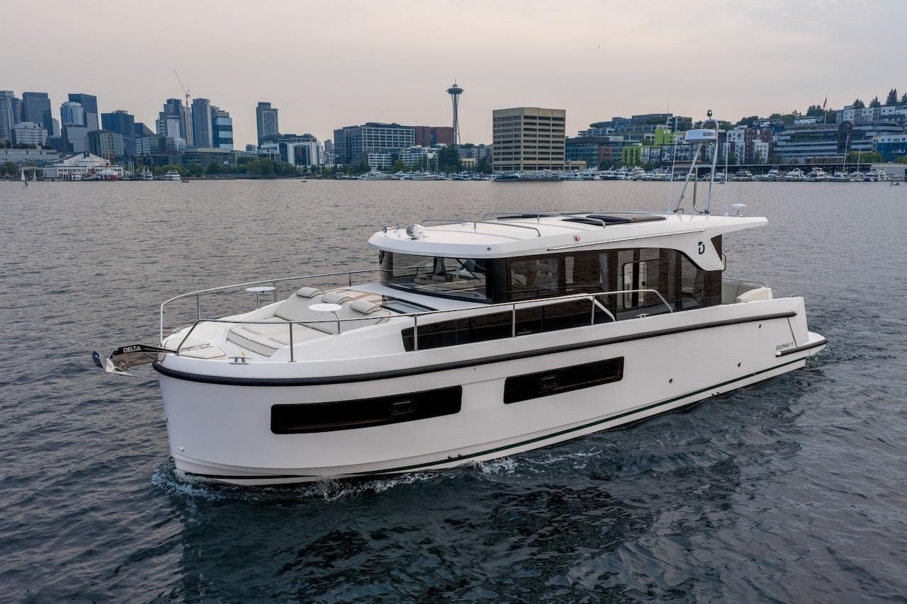 2025 Delphia D11 SEDAN yacht cruising near a city skyline on calm waters.