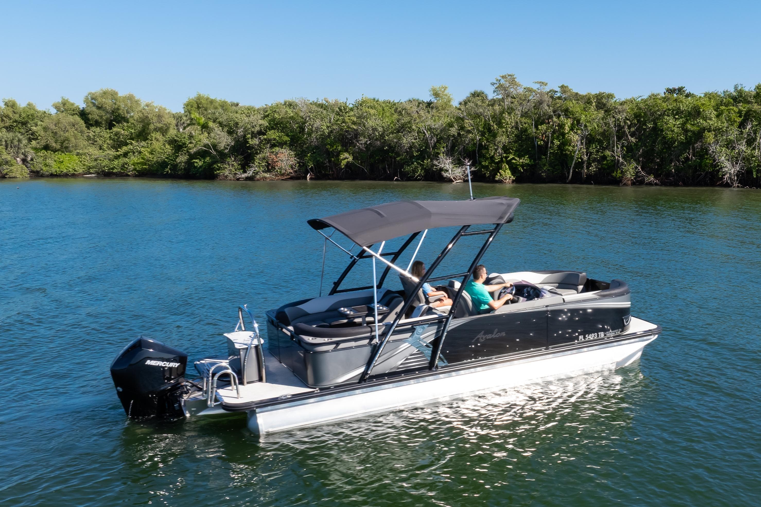 2021 Avalon LSZ Quad Lounger boat cruising on a serene lake with lush greenery.