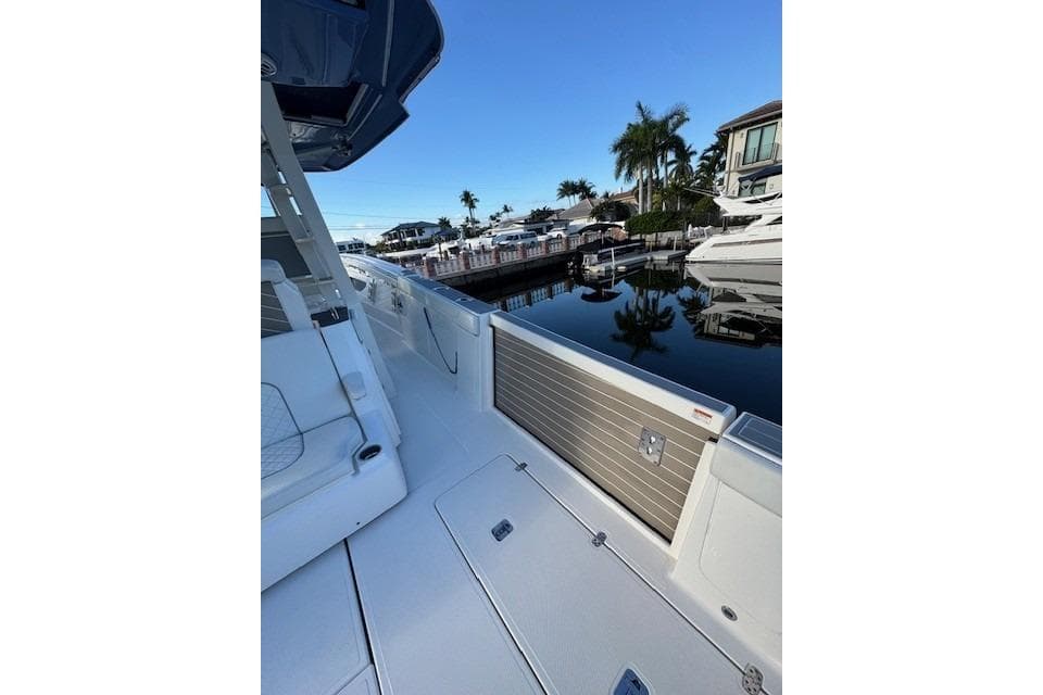 2023 Pursuit S 428 Sport boat docked by waterfront homes and palm trees.