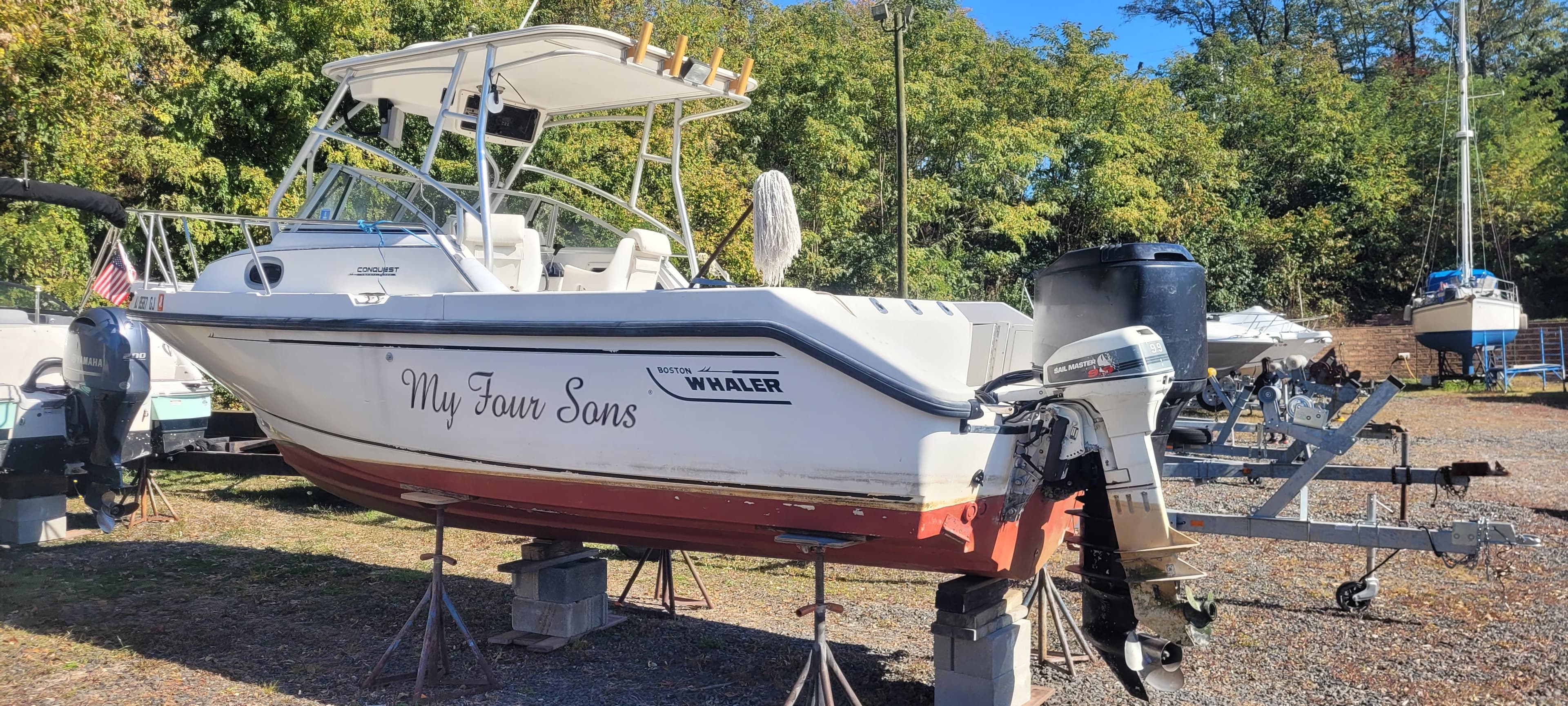 1999 Boston Whaler 23 Conquest boat on stands, named "My Four Sons," in a boatyard.