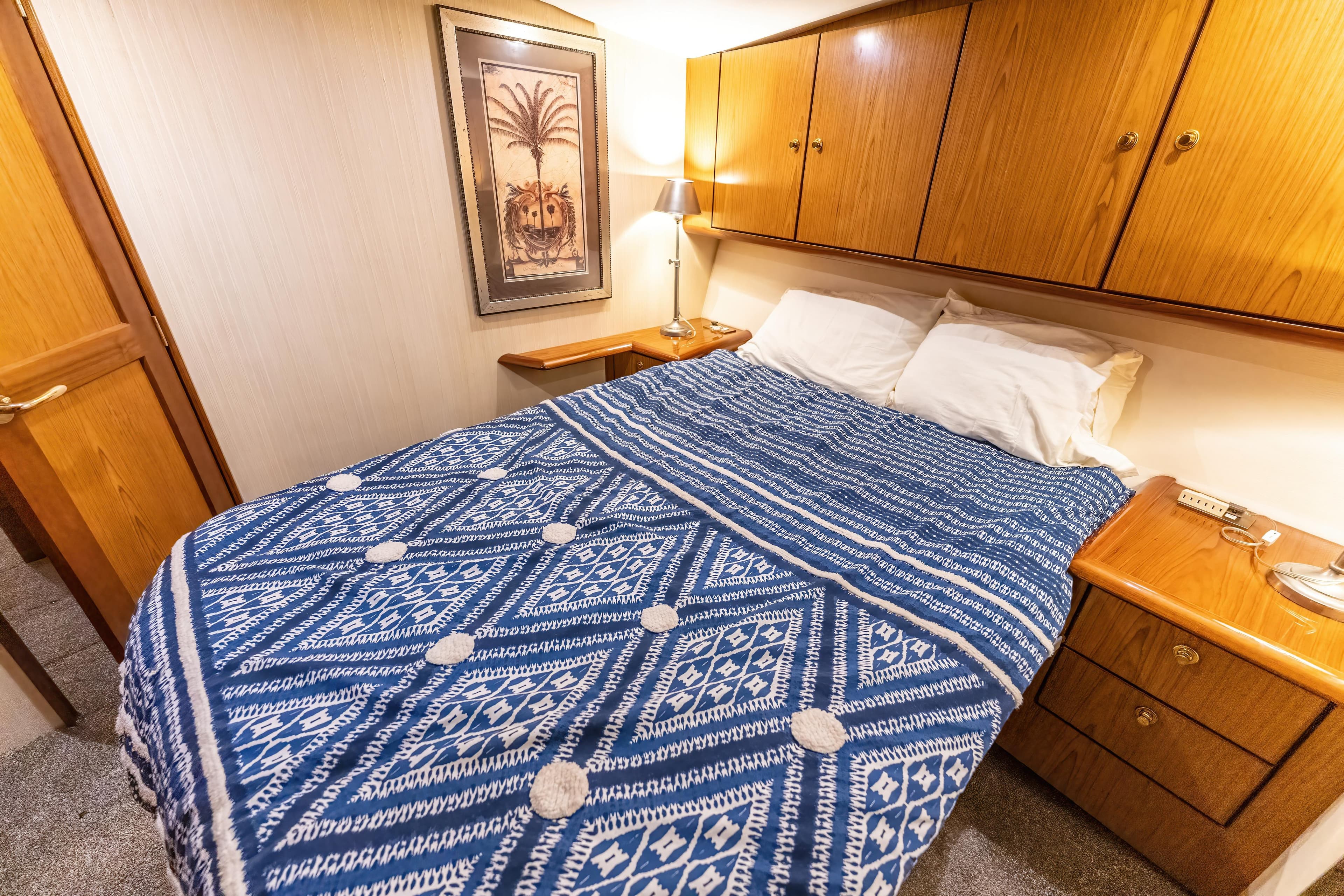 Cozy bedroom in 2006 Ocean 57 yacht with blue patterned bedding and wooden cabinets.