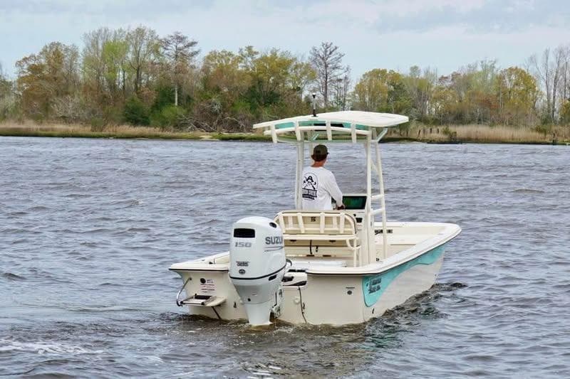 2024 Carolina Skiff 23 LS boat cruising on a river with a Suzuki outboard motor.
