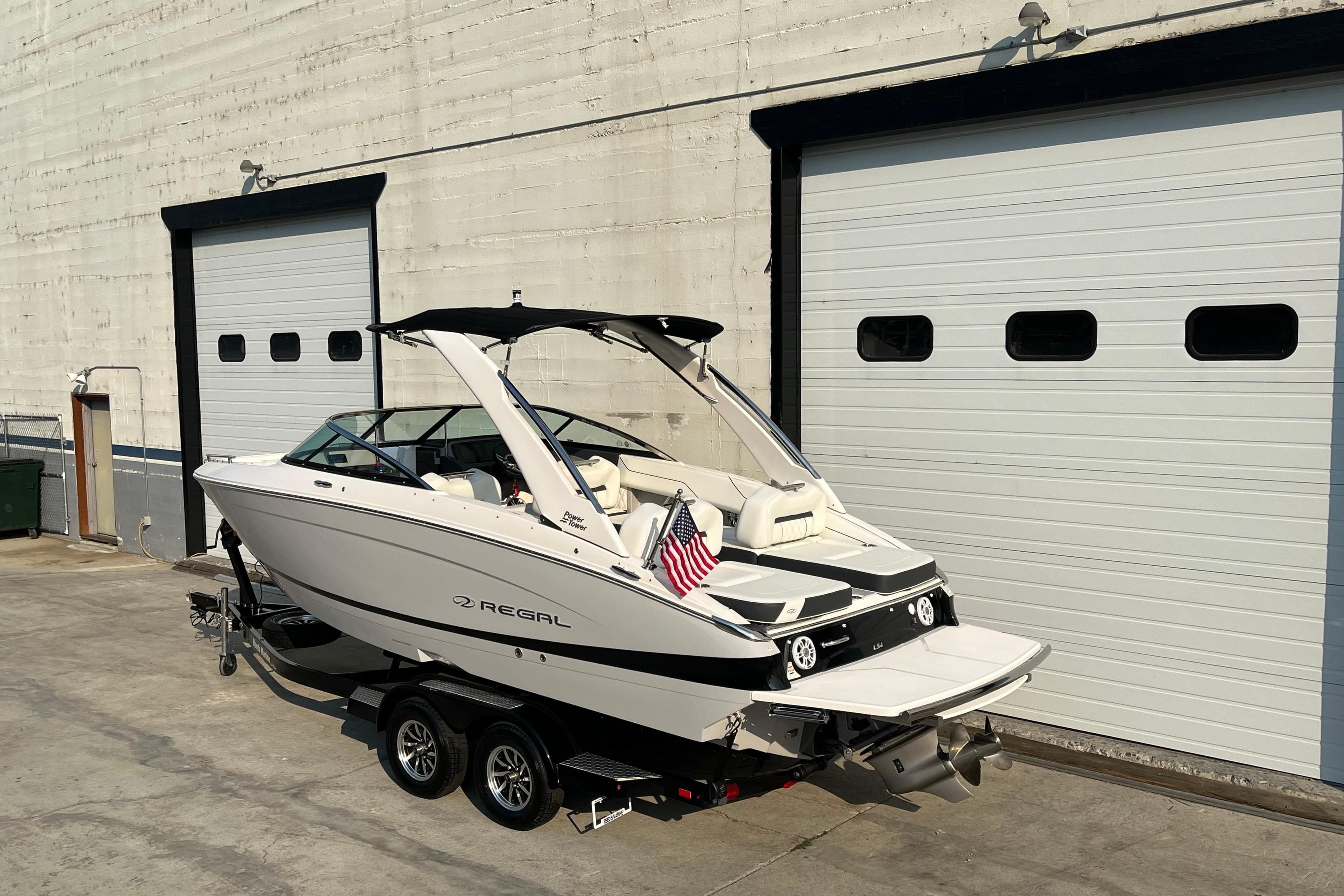 2025 Regal LS4 boat on trailer, parked outside large garage doors.